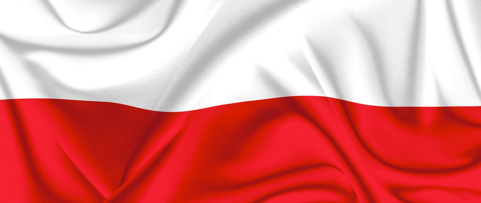 Na fotografii powiewająca flaga Polski składająca się z dwóch połączonych prostokątów - białego na górze, czerwonego na dole.