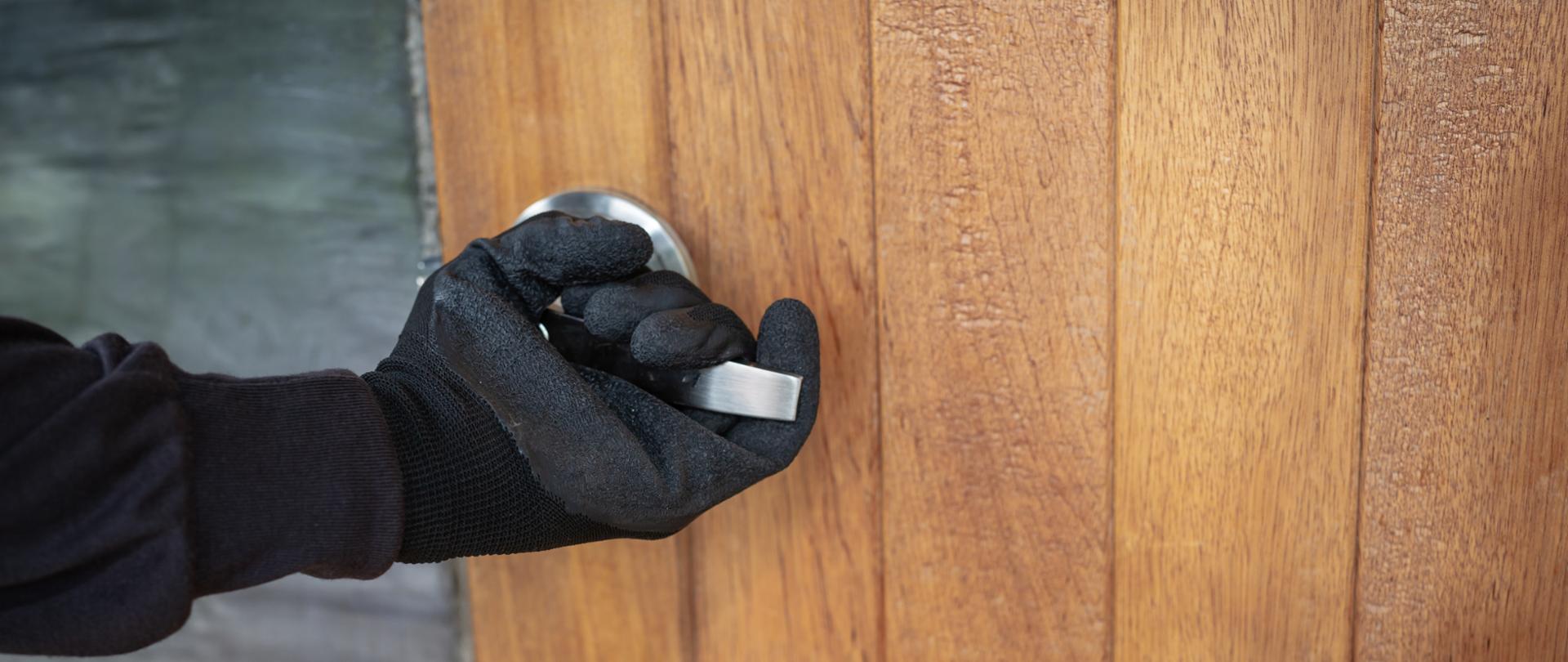Widać rękę w czarnej rękawiczce, która trzyma klamkę otwierając drzwi