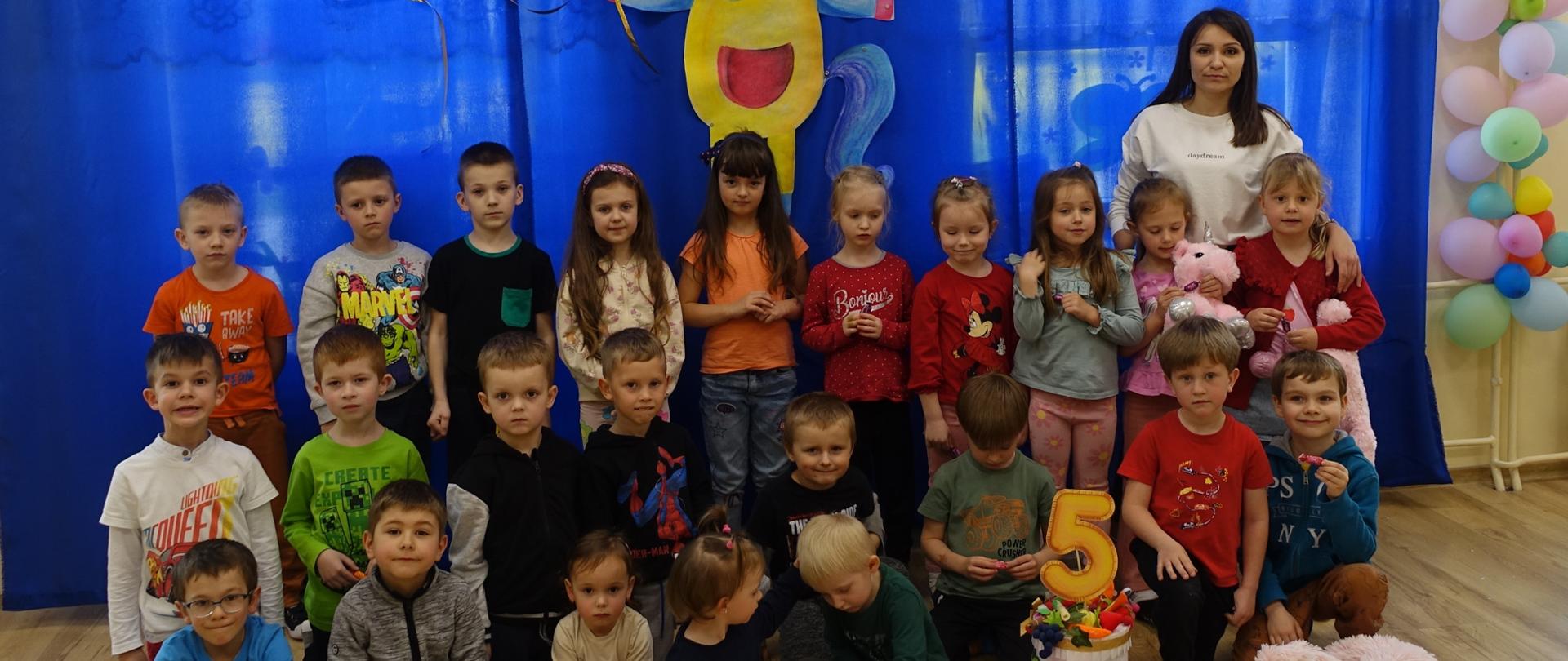 Zdjęcie grupowe przedszkolaków na tle dekoracji przedstawiającej jednorożca Felusia. 
