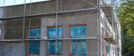 Budynek przyszykowany do malowania posiada przed sobą rusztowanie oraz na oknach jest folia zabezpieczeniowa przed pomalowaniem szyb.