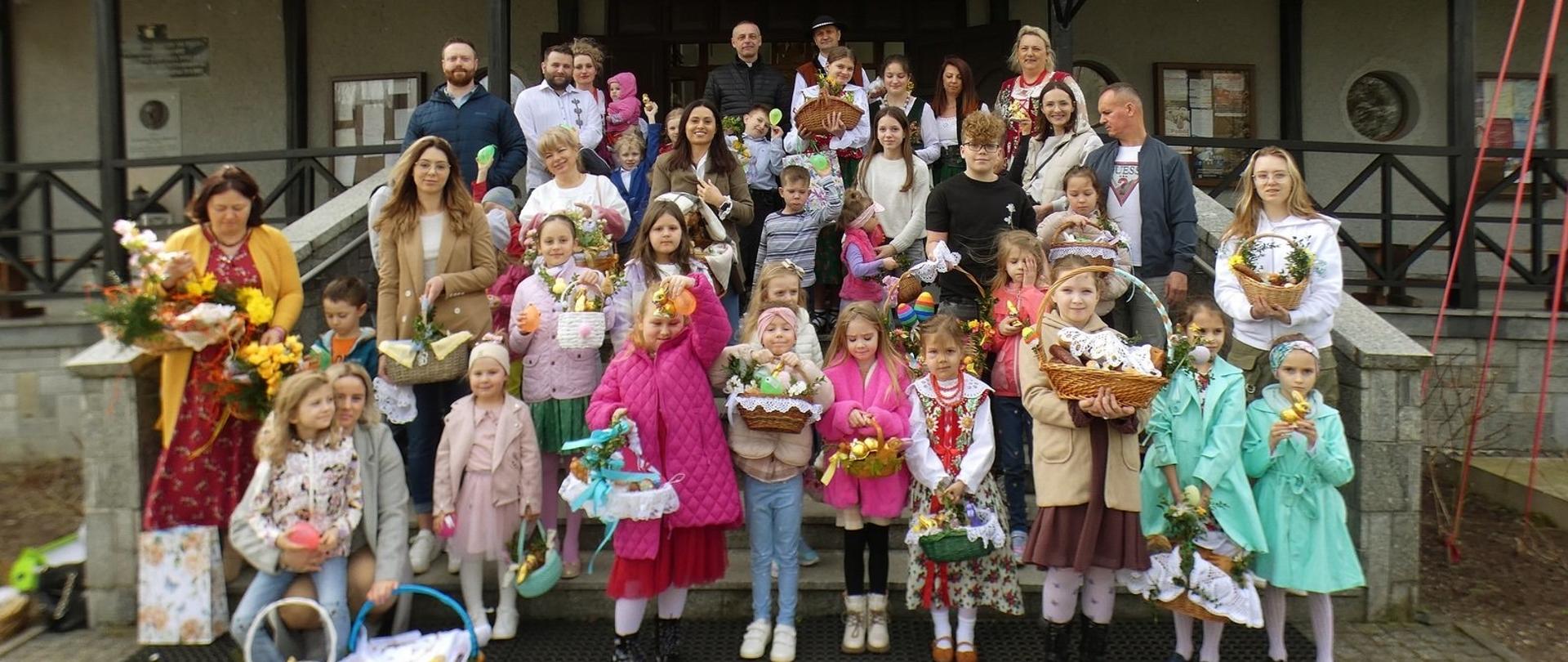 Zdjęcie przedstawiający na tle kościoła uczestników konkurs na Najpiękniejszy Koszyczek Wielkanocny w Sieniawie 