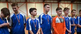 Grupka chłopców stoi na sali gimnastycznej, spoceni oraz mają na szyjach medale oraz parę osób trzyma dyplomy, gratulacyjne wystąpienia w zawodach sportowych.