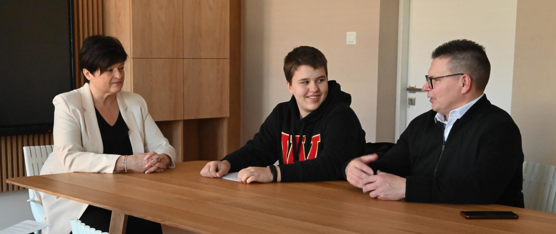 Sekretarz Miasta wraz z uśmiechniętą Barbarą Karolak i trenerem Jerzym Jaśniakiem siedzą przy stole