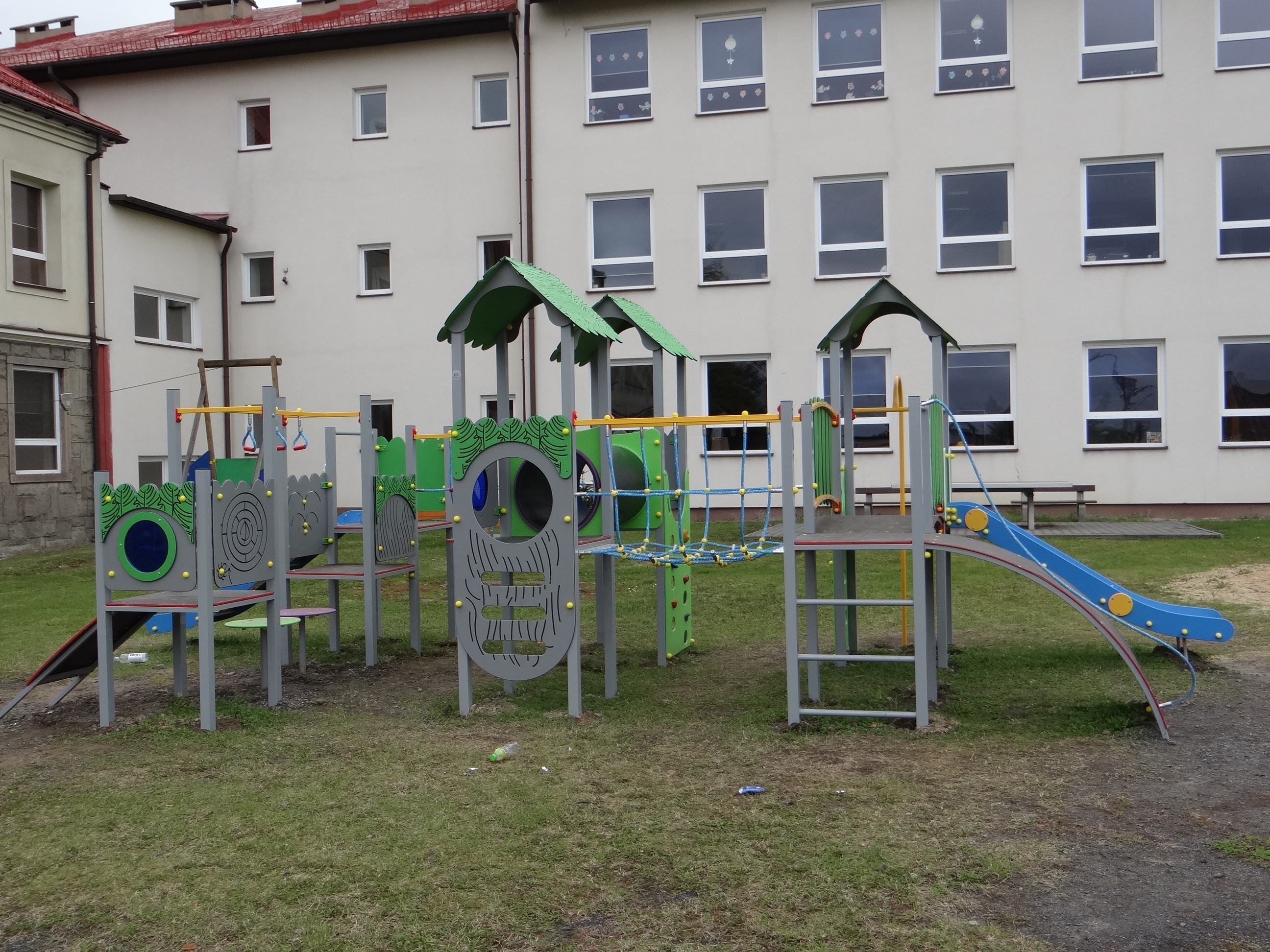 Ogólnodostępny plac zabaw przy Szkole Podstawowej w Pogwizdowie po modernizacji (1). Widoczna część urządzeń placu. Z tyłu budynek szkolny (skrzydło wschodnie i częściowo północne).