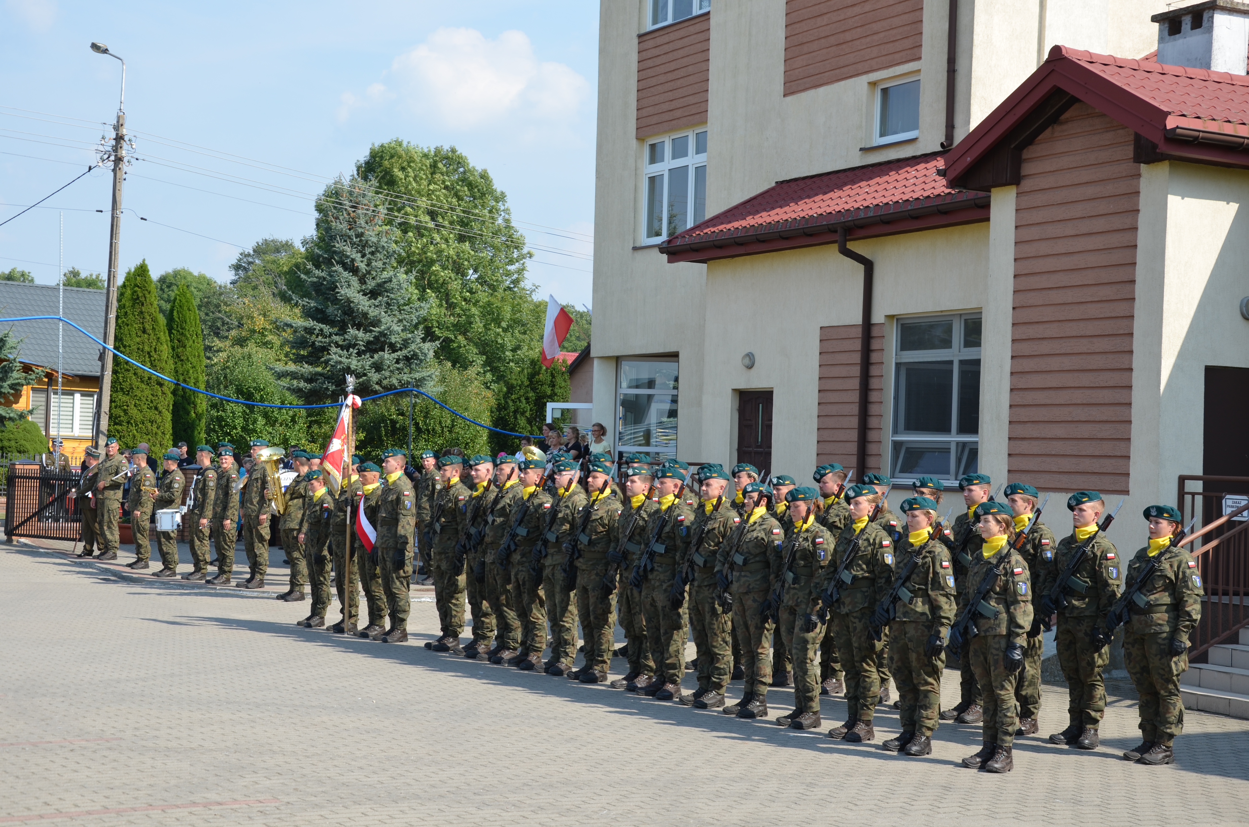 Żołnierze w mundurach z bronią na ramieniu stoją w dwuszeregu.
