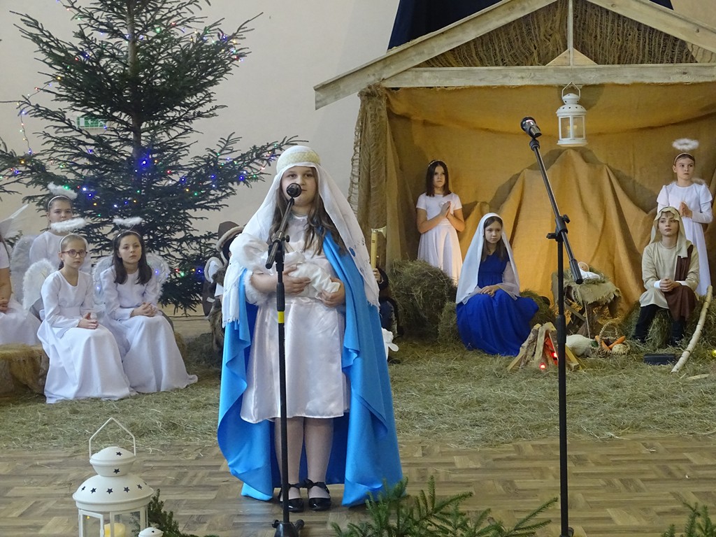 Zdjęcie przedstawia dziewczynkę przebraną za Maryję, na rękach trzyma malutkiego Jezusa jednocześnie wykonując przygotowany utwór w Gminnym Przeglądzie Kolęd i Pastorałek. 
