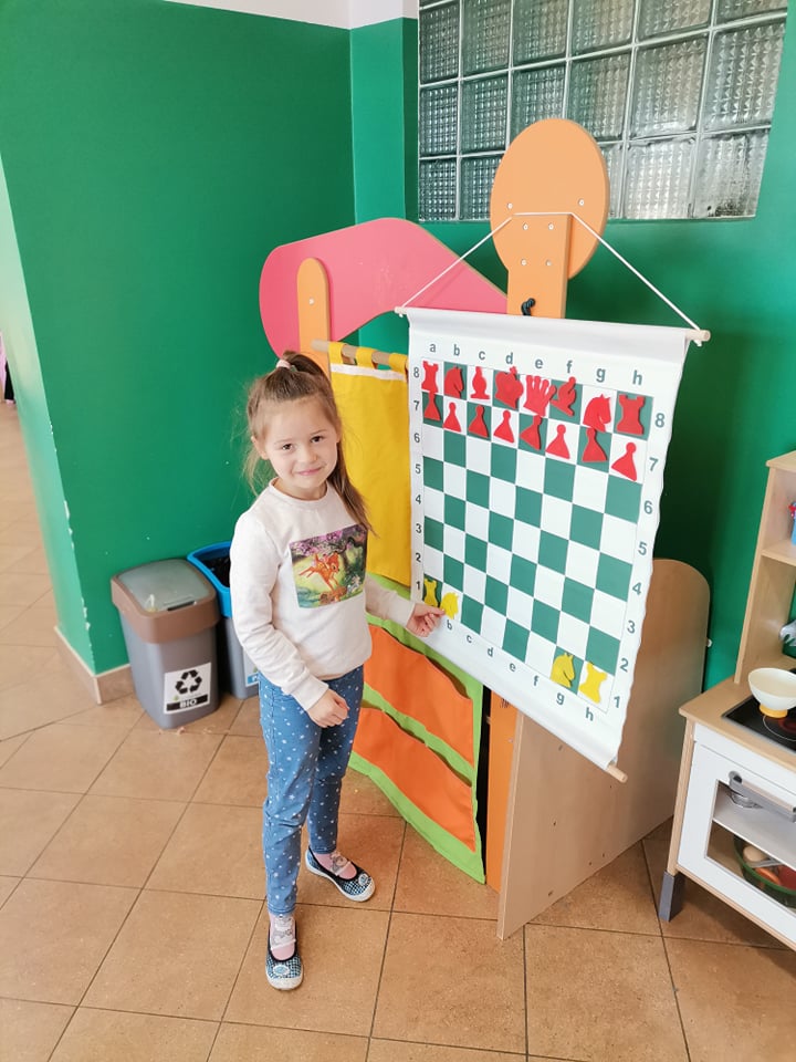 Dziewczynka stoi przy wiszącej szachownicy 