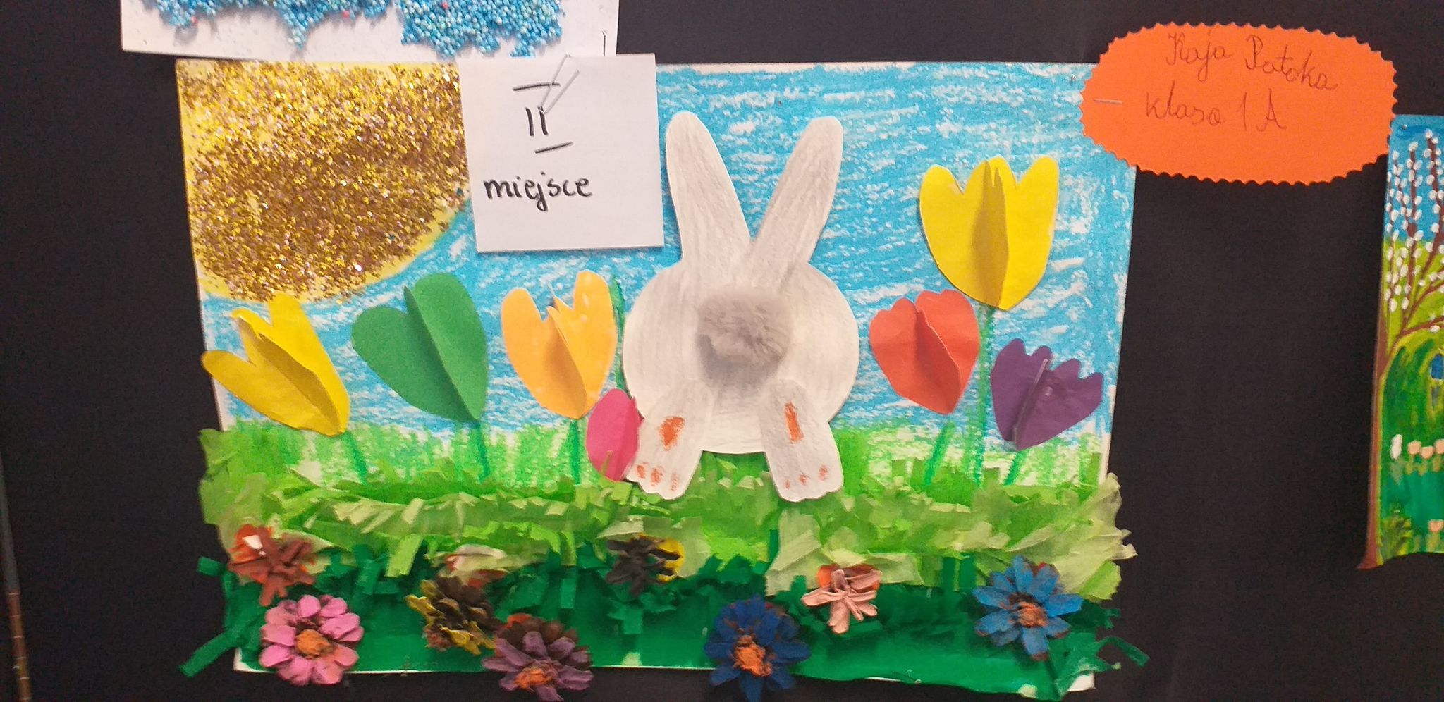 Obrazek z białym królikiem z puchatym ogonem, kwiatami z papieru i łąką