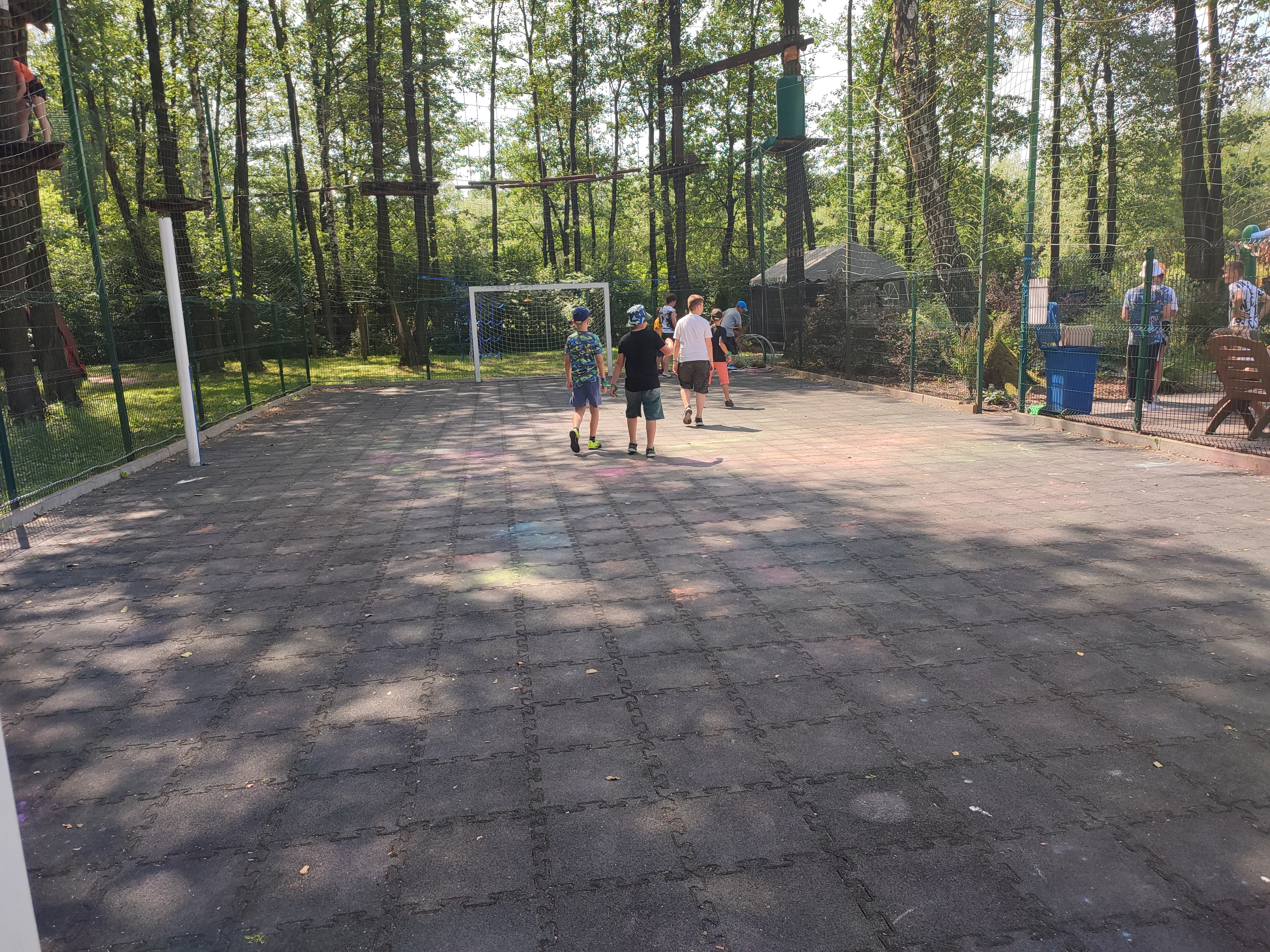 Zdjęcie przedstawia kilkoro dzieciaków grających w piłkę na placu Parku Linowego.