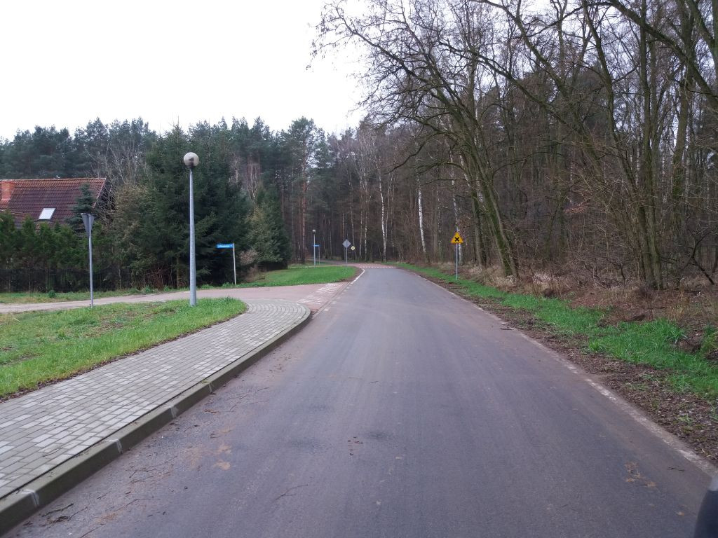 asfaltowa droga gminna nr 198015P Rutki-Klotyldzin, po prawej las, po lewej chodnik z kostki brukowej