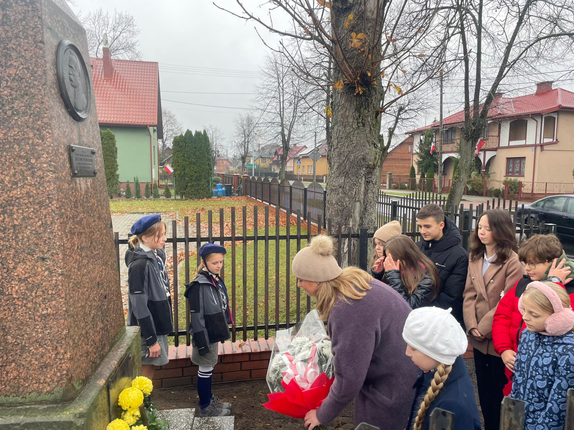 Dyrektor szkoły wraz z uczniami podczas złożenia kwiatów przy pomniku Józefa Piłsudzkiego w Porębie.