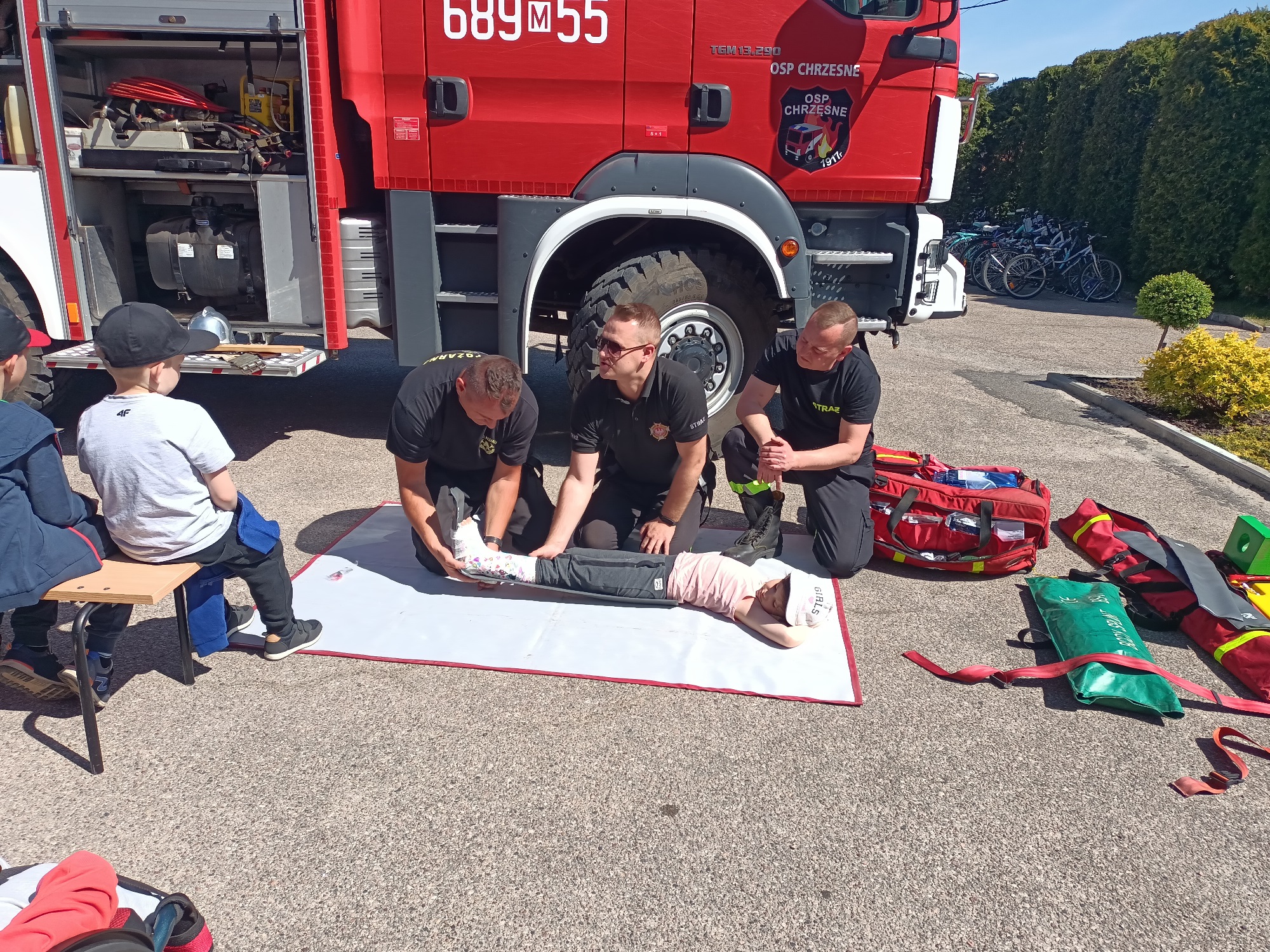 Dwoje strażaków schylających się nad dzieckiem z nogą w bandażu