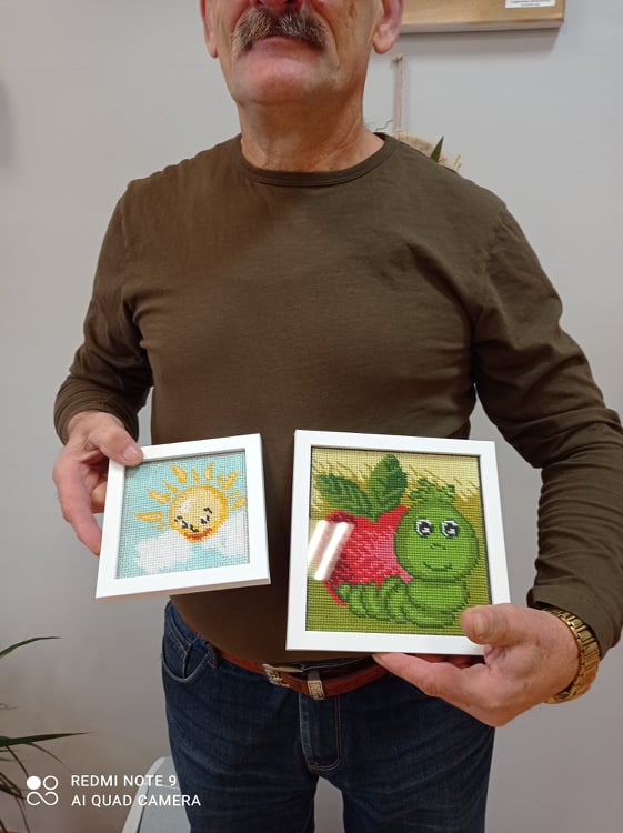 Mężczyznę w wieku od 70 do 80 lat trzymającego obrazki wykonane z włóczki.