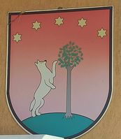 Herb Bukowiny Osiedla przedstawiający wilka opartego na bukach, a nad nim w półkolu pięć gwiazd. 