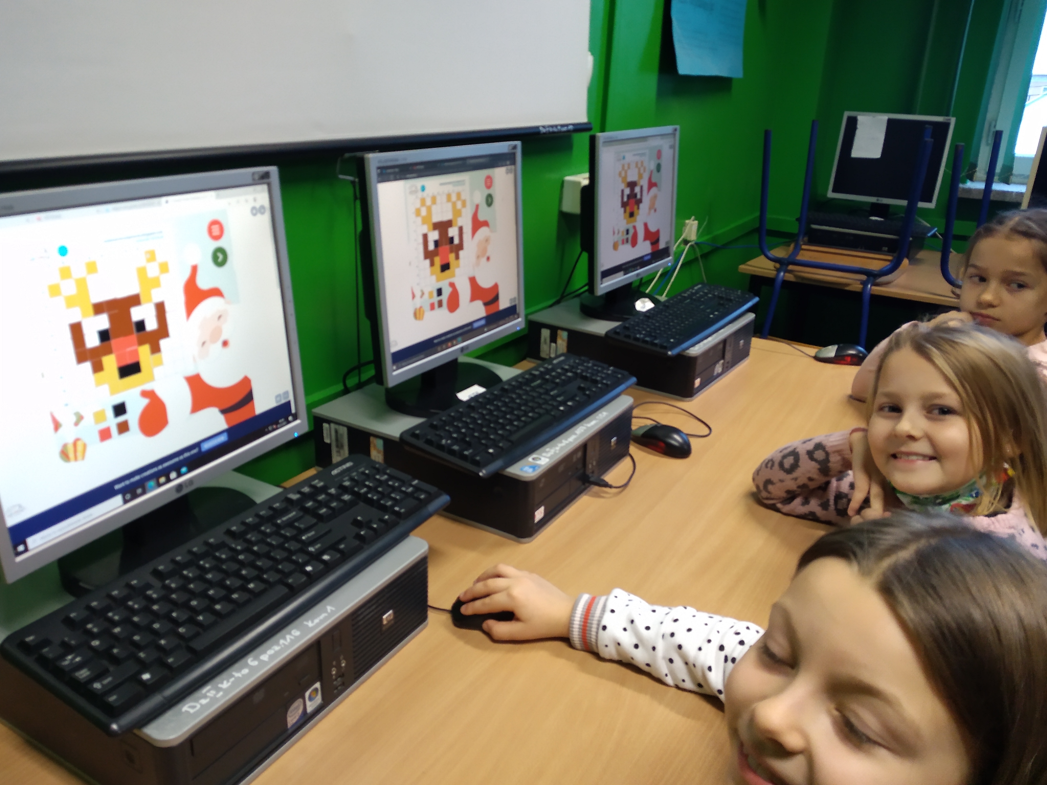 Dzieci układają na ekranach komputerów obrazki renifera z kolorowych kwadratów