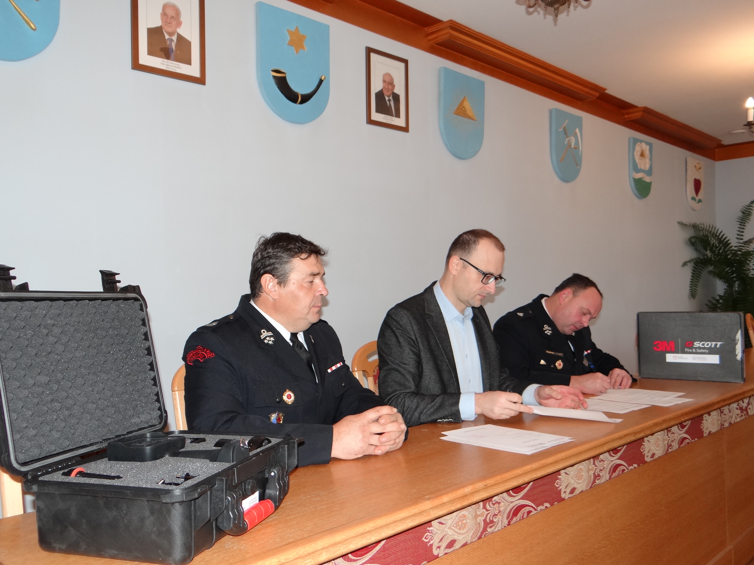 Podpisanie umowy darowizny pomiędzy Gminą Hażlach a Ochotniczą Strażą Pożarną w Hażlachu. Trzy osoby, w tym dwóch strażaków w mundurach, podpisują dokumenty