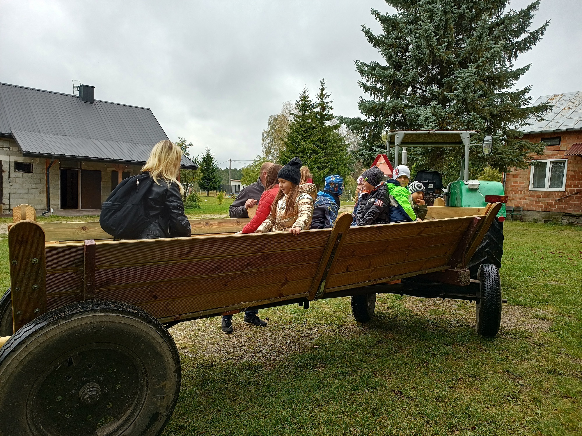 Dzieci siedzą w drewnianym wozie ciągniętym przez traktor