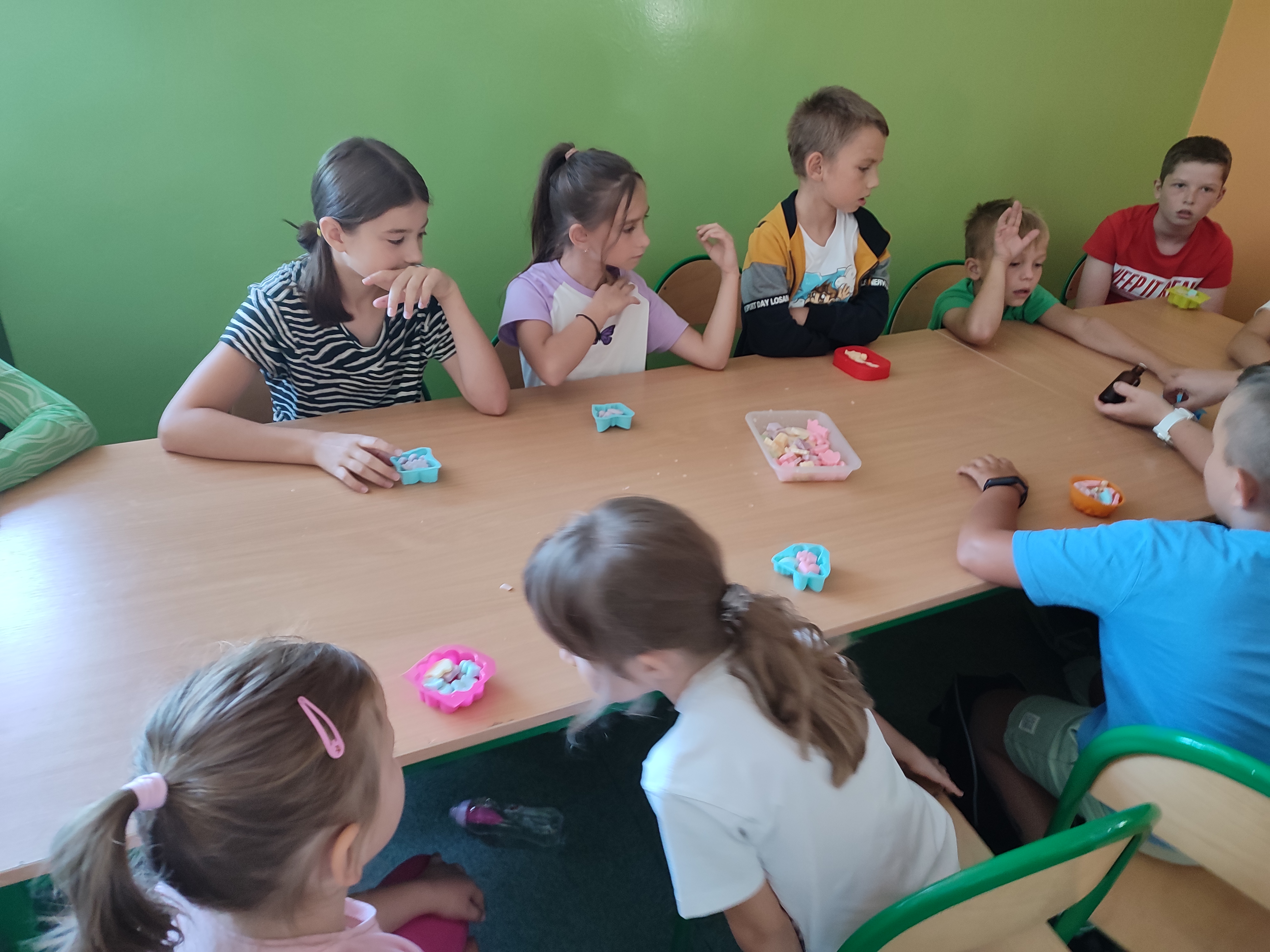 Zdjęcie przedstawia grupę dzieci wybierających kształty i rzeczy potrzebne do utworzenia mydełka glicerynowego