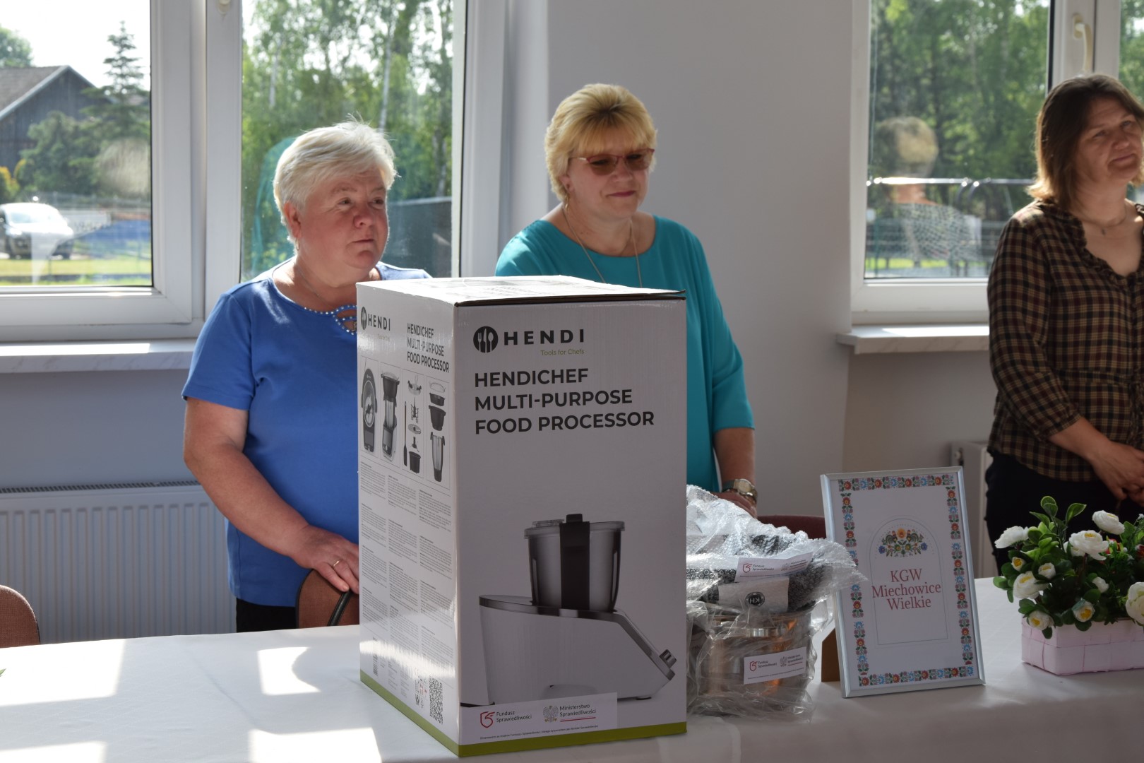 zdjęcie przedstawia trzy kobiety w wieku od 50 do 60 lat stojące za stołem, na stole znajdują się sprzęt i akcesoria kuchenne.