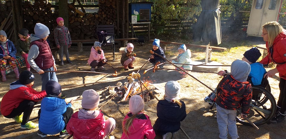 Dzieci kucają wokół ogniska i pieką na kijach kiełbaski