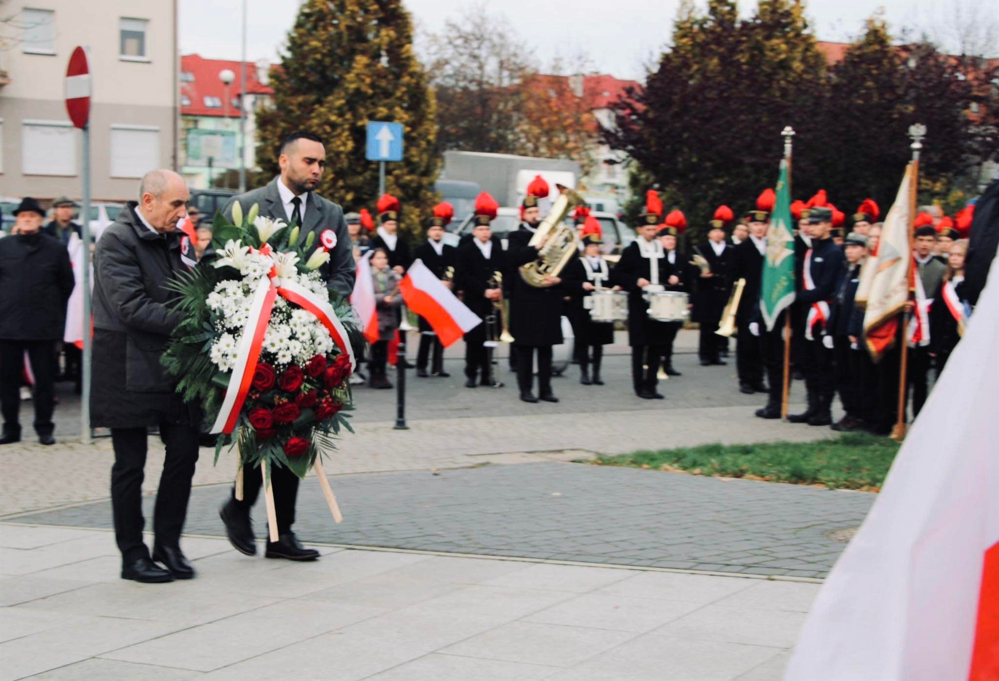 Władze powiatu polkowickiego niosą wieniec z kwiatami pod pomnik podczas obchodów święta niepodległości