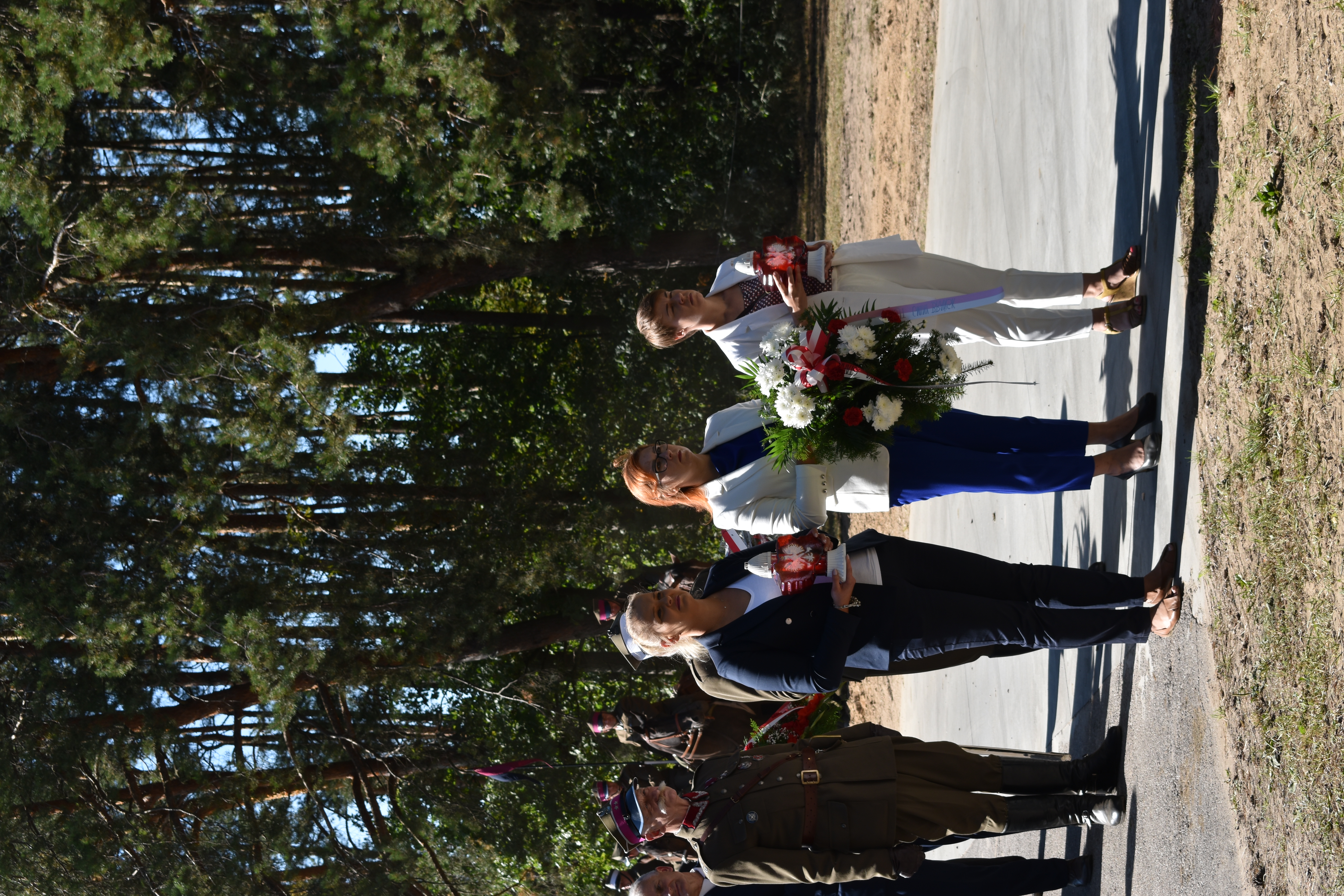 Trzy kobiety w rekach trzymają znicze i kwiaty w biało- czerwonych barwach