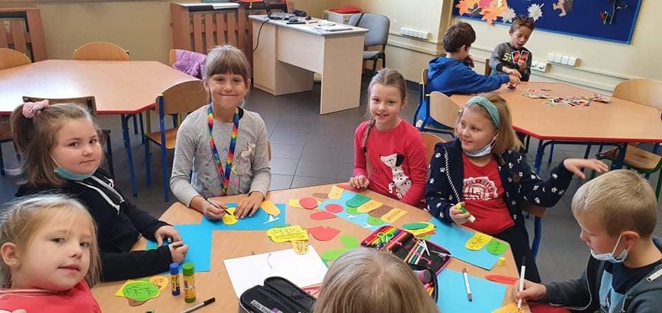 Dzieci siedzą przy soliku i wyklejają kolorowe obrazki z papieru kolorowego