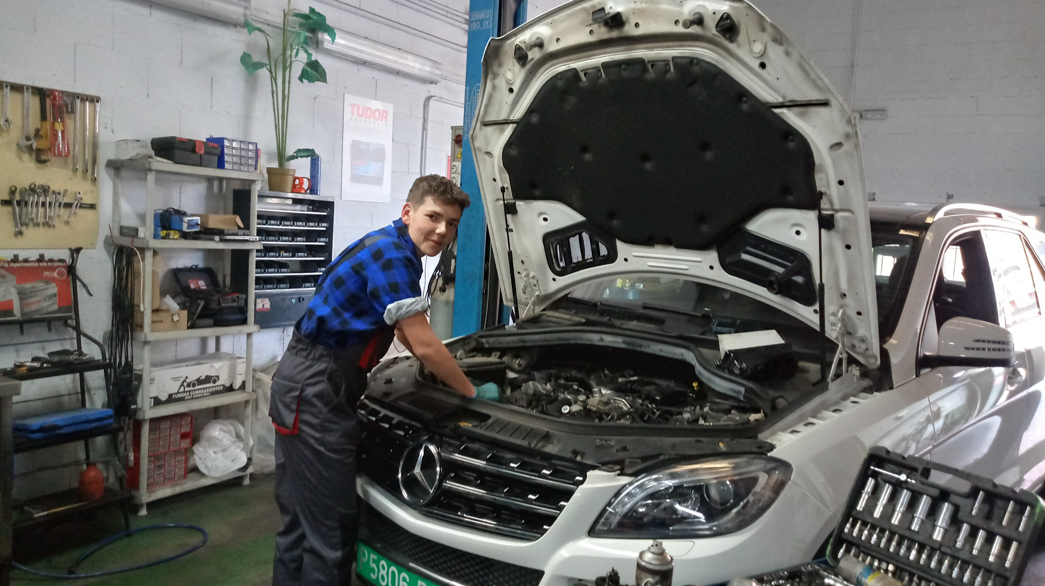 Młody mężczyzna w stroju mechanika naprawia biały samochód marki Mercedes 