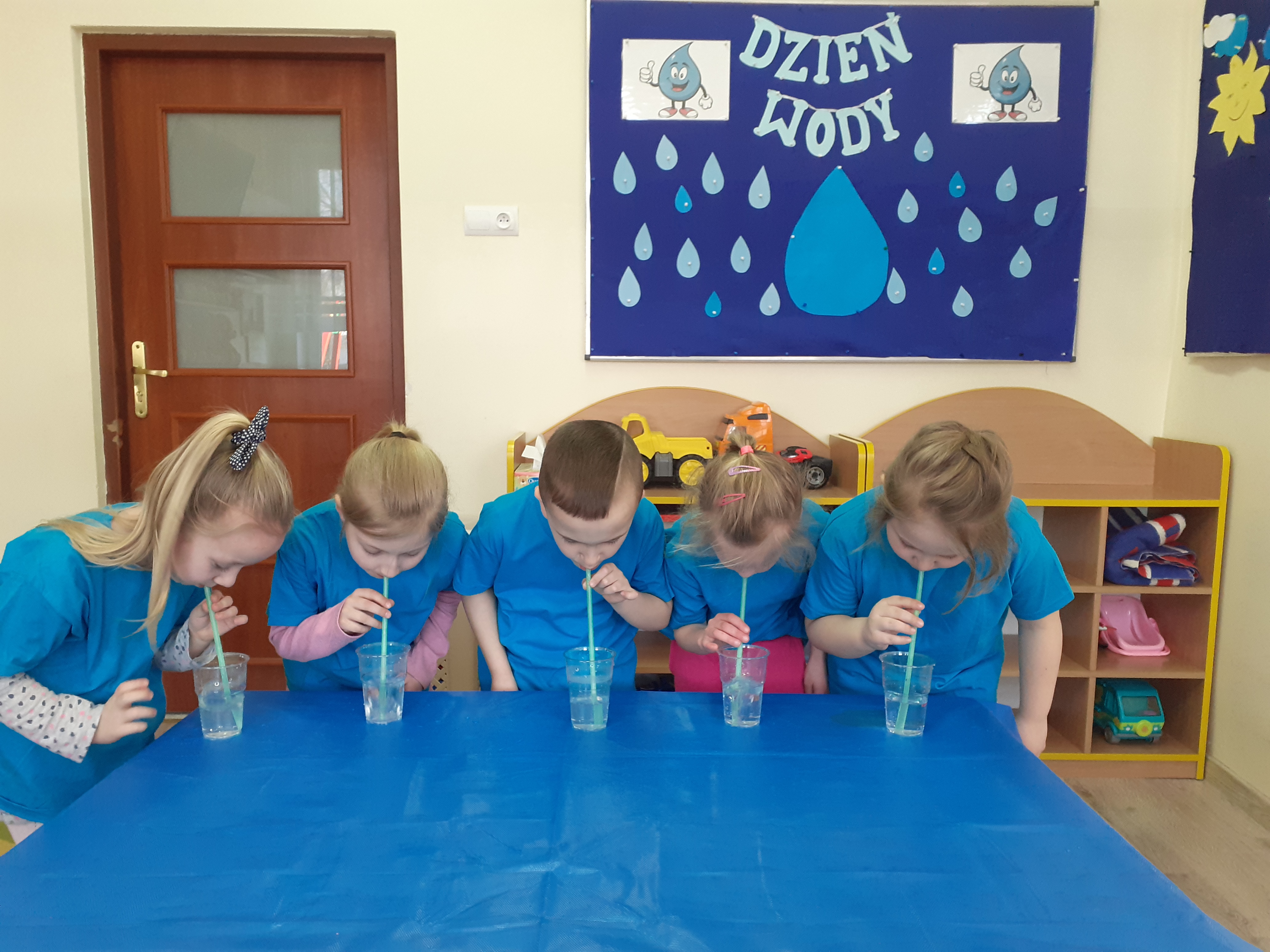 Dzieci dmuchają przez rurki do plastikowych kubeczków z wodą