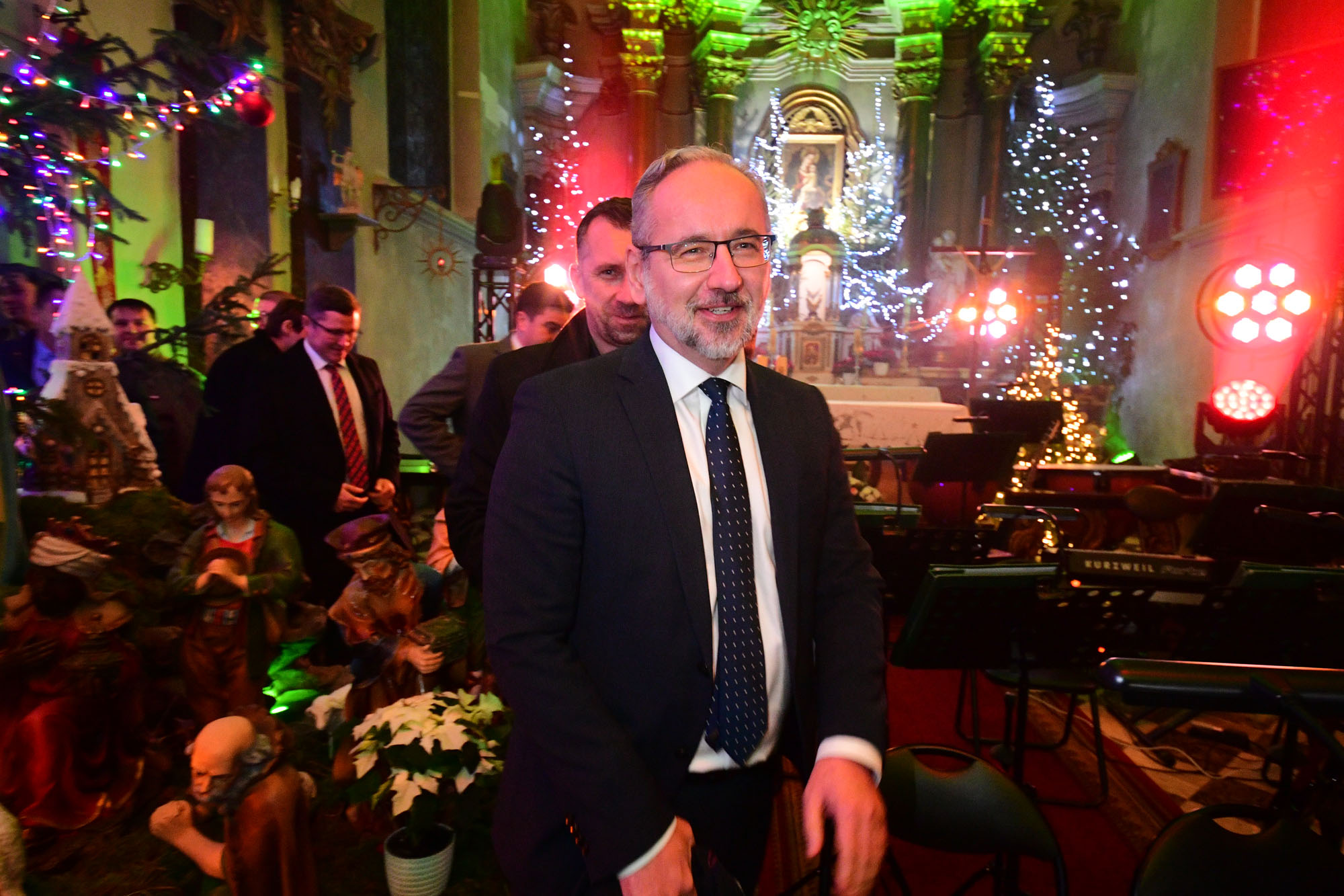 Minister Adam Niedzielski na pierwszym planie w kościele w Margoninie, za nim ołtarz podświetlony światłami i sprzęt orkiestry.