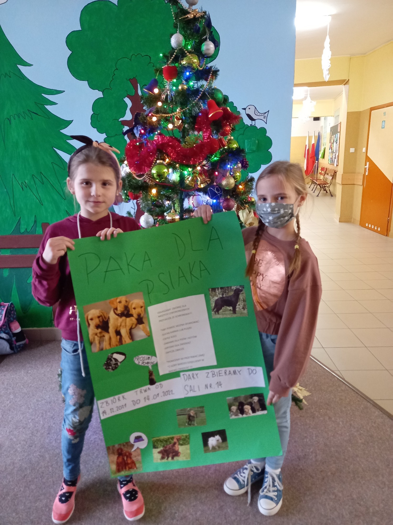 Dwie dziewczynki trzymają dużą zieloną kartę tytułem Paka dla psiaka ze zdjęciami psów
