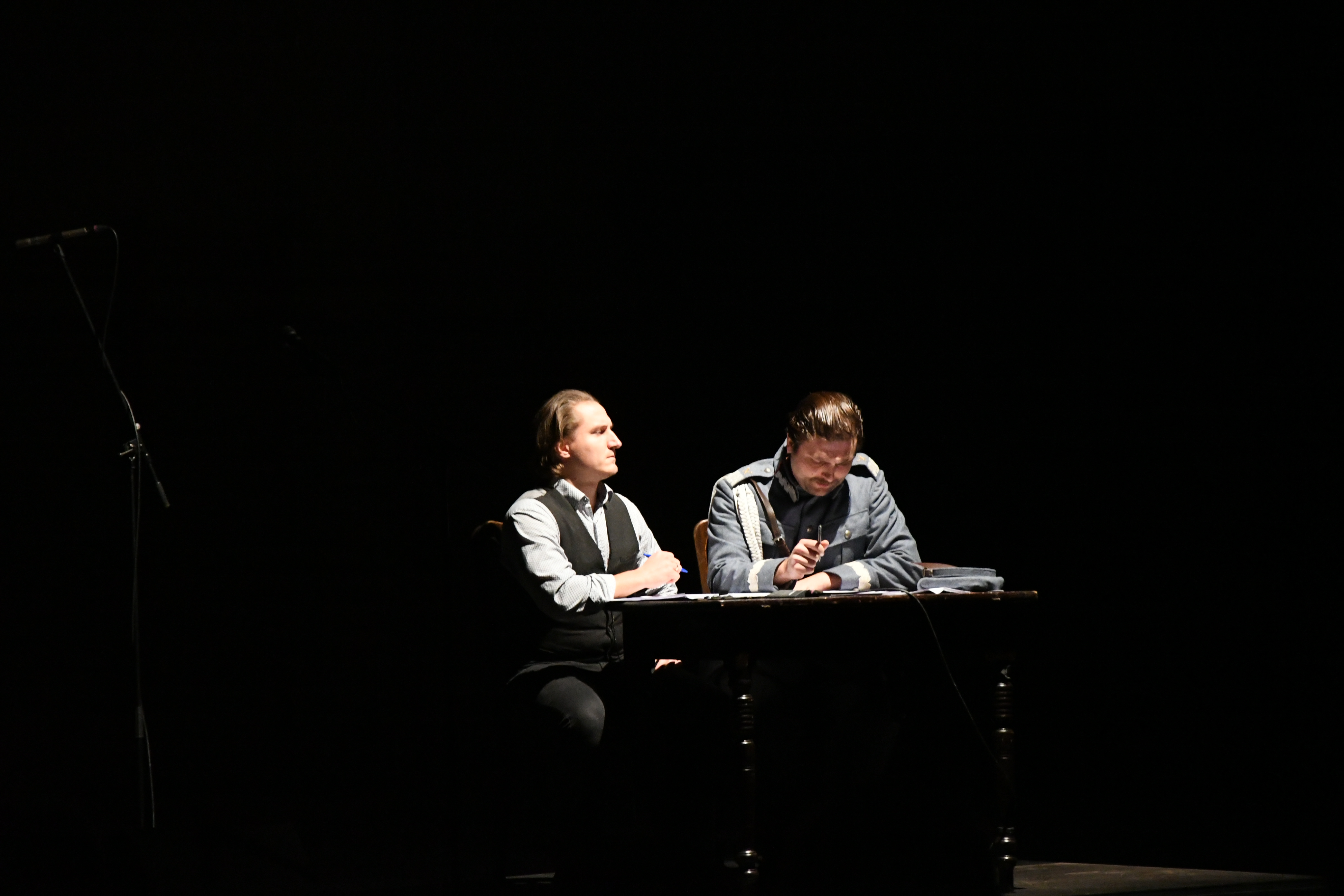 Dwie osoby siedzą przy biurku na scenie.