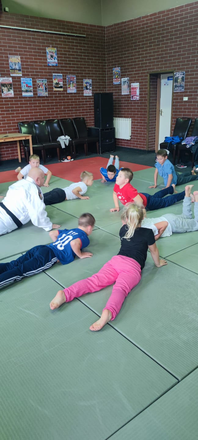 dzieci i trener ćwiczące na zielonych matach rozłożonych na podłodze