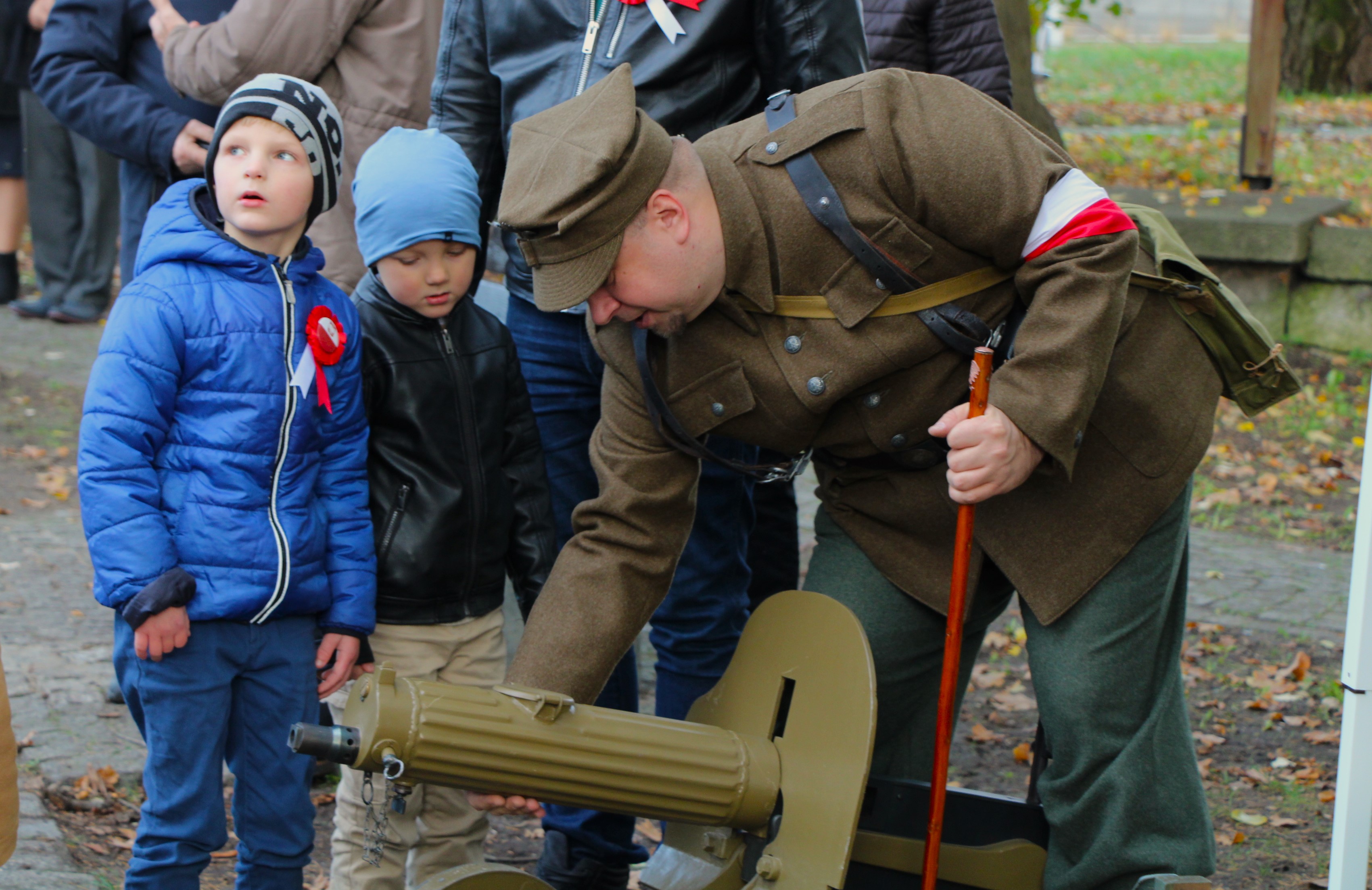 mężczyzna ubrany w strój wojskowy pokazuje dzieciom broń z czasów drugiej wojny światowej 
