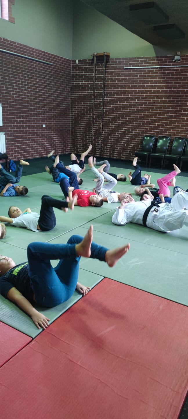 dzieci i trener ćwiczące na zielonych i czerwonych matach rozłożonych na podłodze