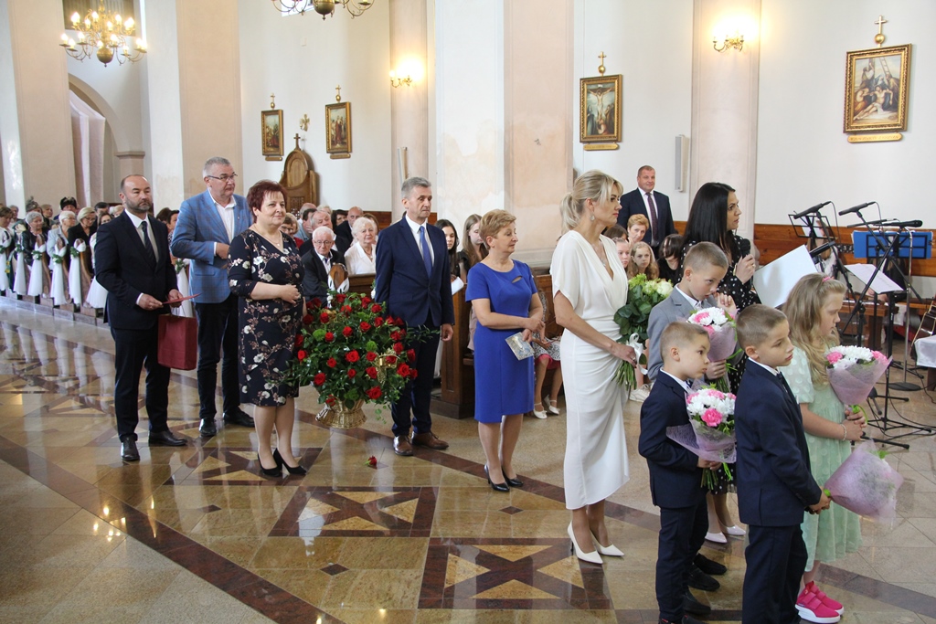 Grupa osób z kwiatami oraz upominkami w trakcie składania życzeń jubilatowi