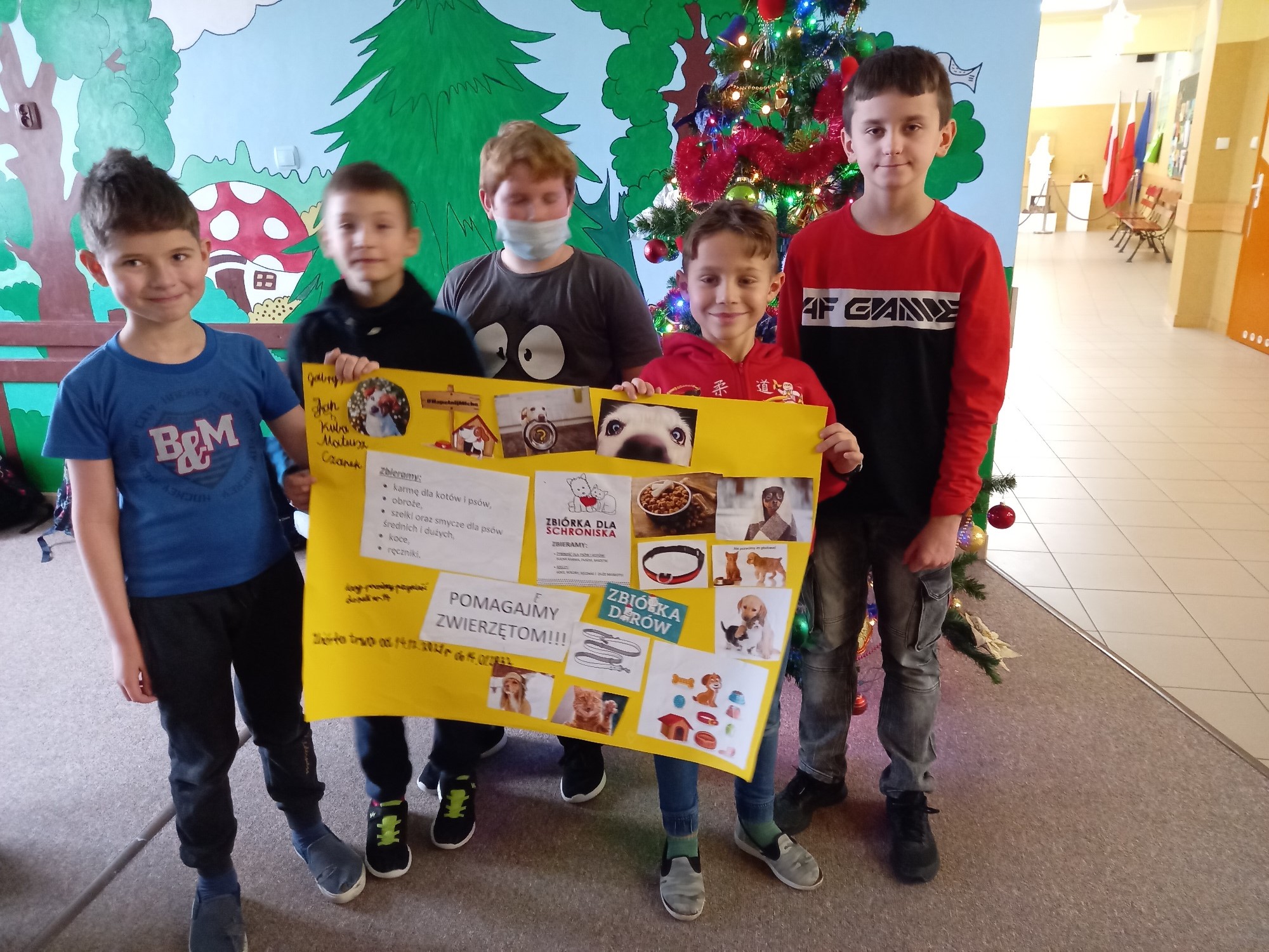 Chłopcy trzymają dużą żółtą kartę z tytułem pomagamy zwierzętom