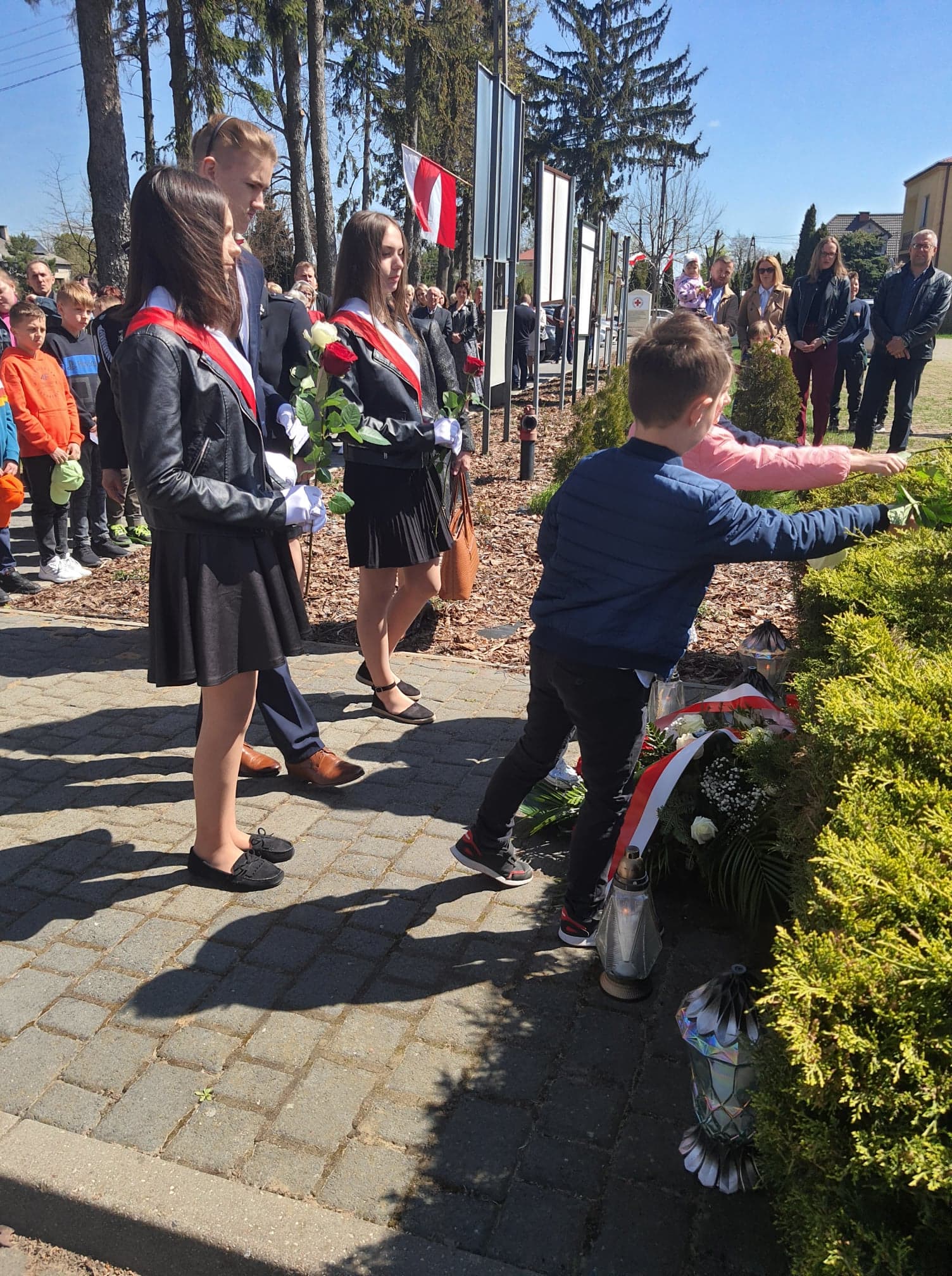 Dzieci i młodzież szkolna składają pod pomnikiem kwiaty w barwach biało-czerwonych.