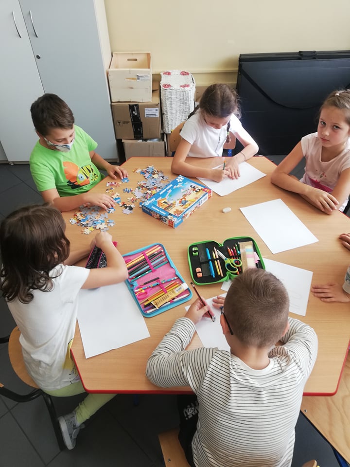 Dzieci siedzą przy stoliku, na którym leżą piórniki i obrazki z papieru kolorowego