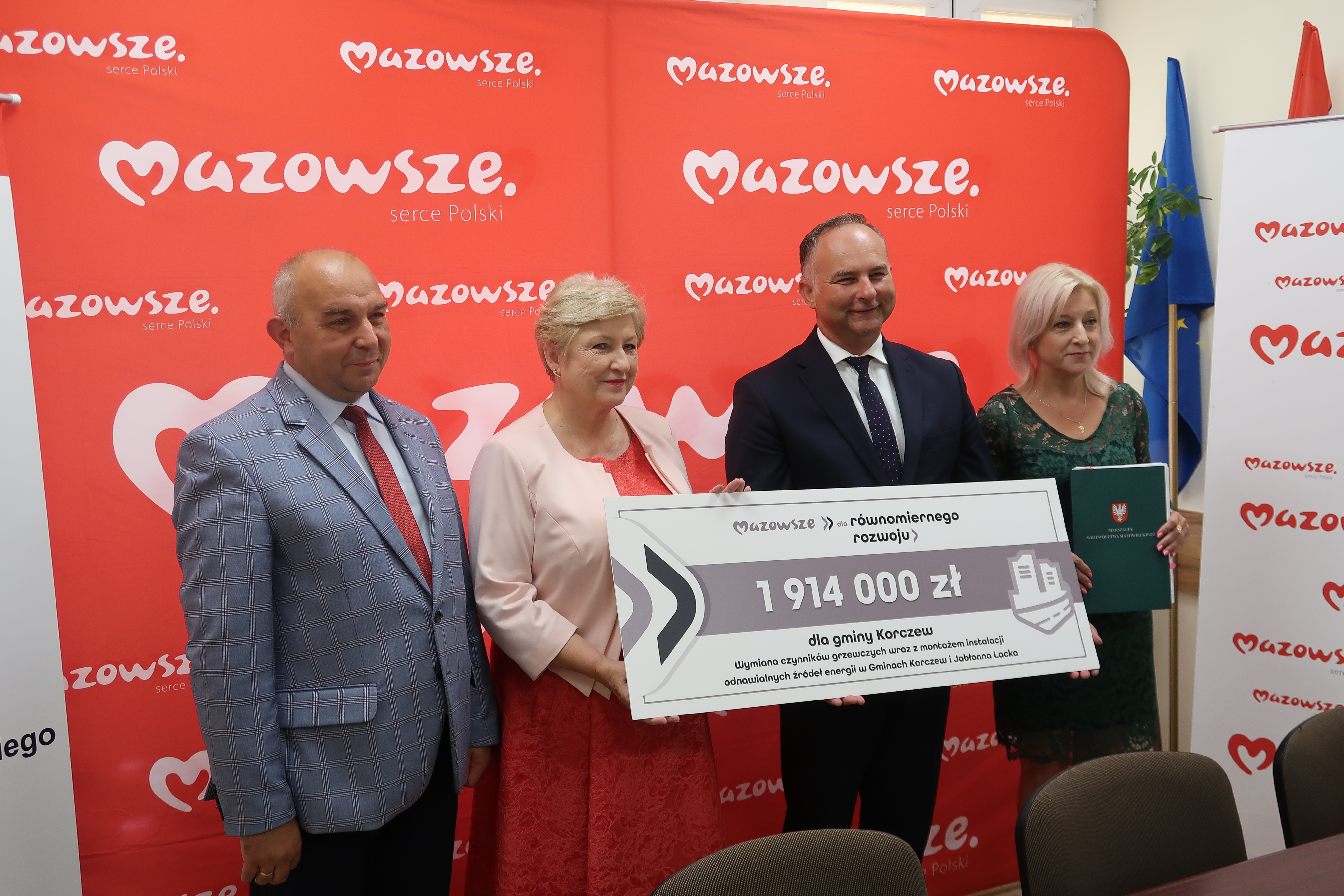  „białe i czerwone tło z logo marki Mazowsze serce Polski oraz herbem województwa mazowieckiego a na tym tle ludzie podpisują dokumenty”