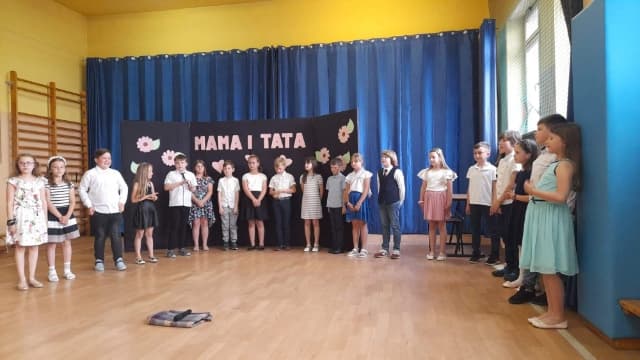 Dzieci ustawione w rzędzie przed tablicą z napisem Mama Tata