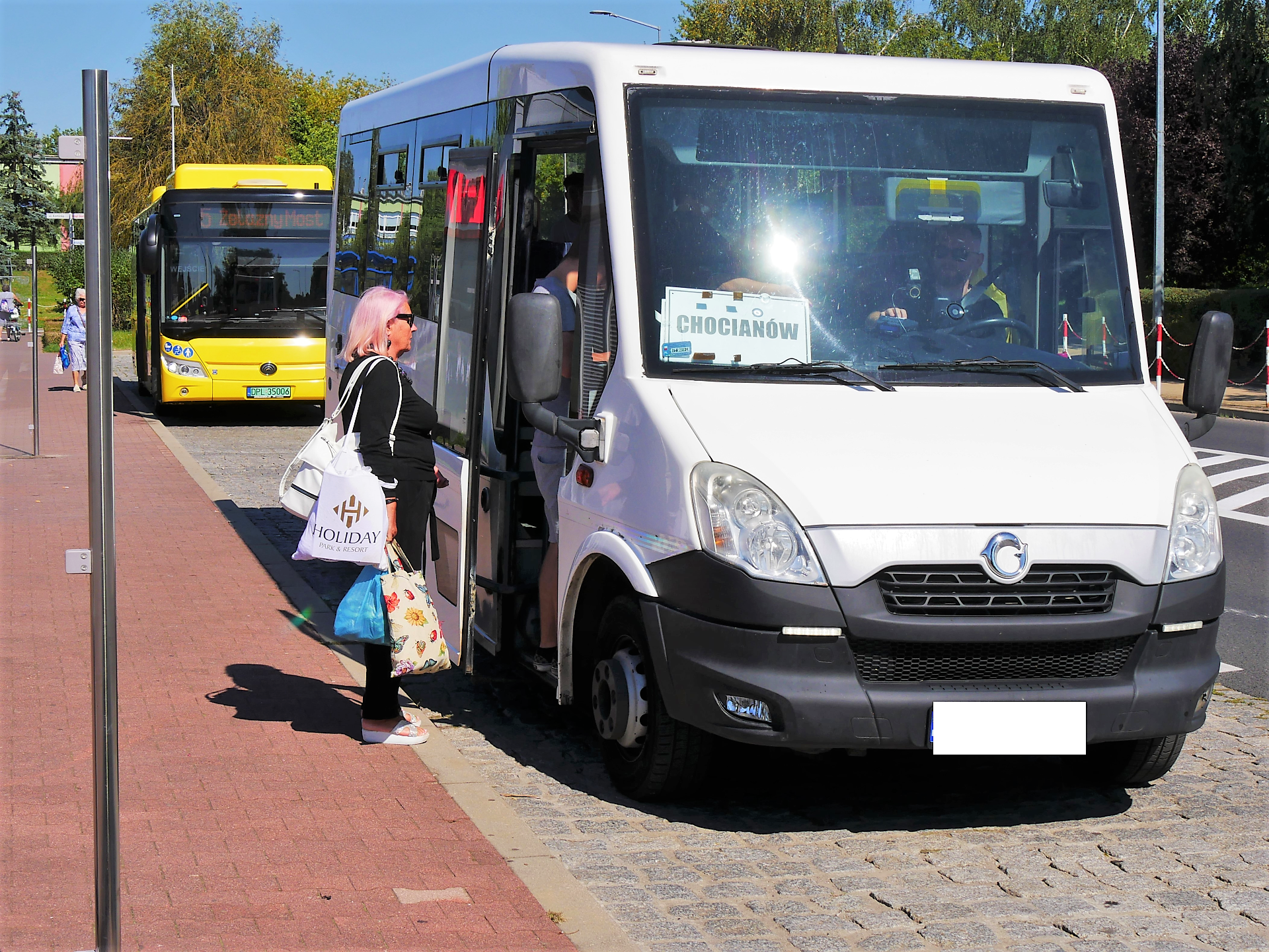 biały bus stoi na przystanku i kobieta wchodzi do niego 