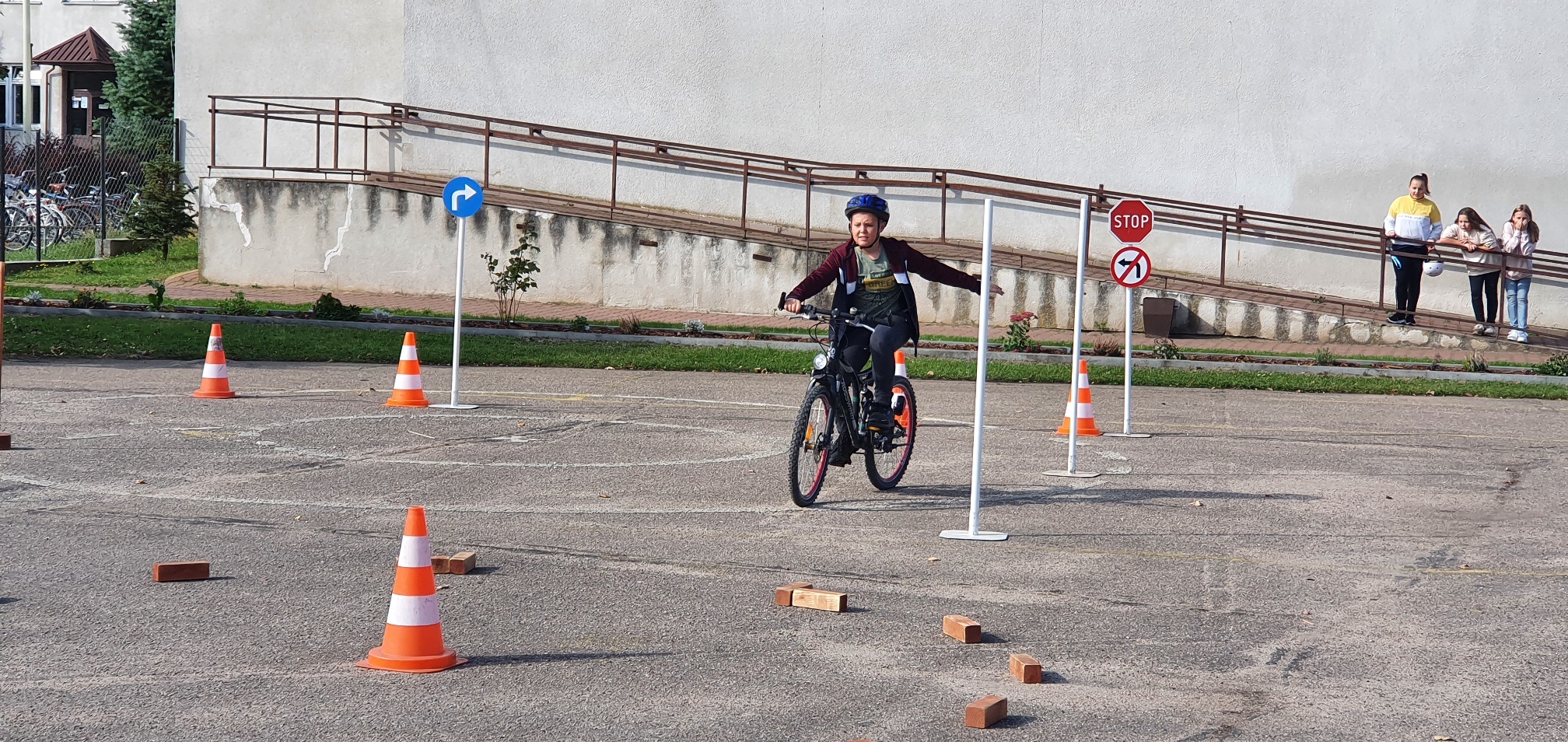 Chłopiec kasku jedzie rowerem po placu, gdzie trasę jazdy wyznaczają cegły i pachołki