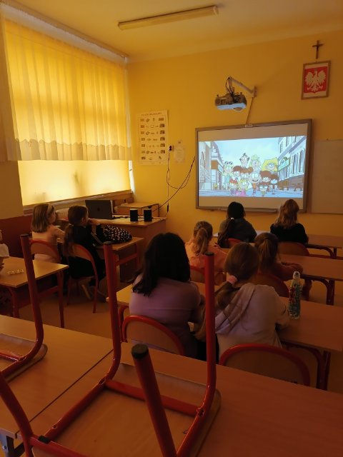 Zdjęcie przedstawia dzieci oglądających bajkę odtworzoną z projektora. 
