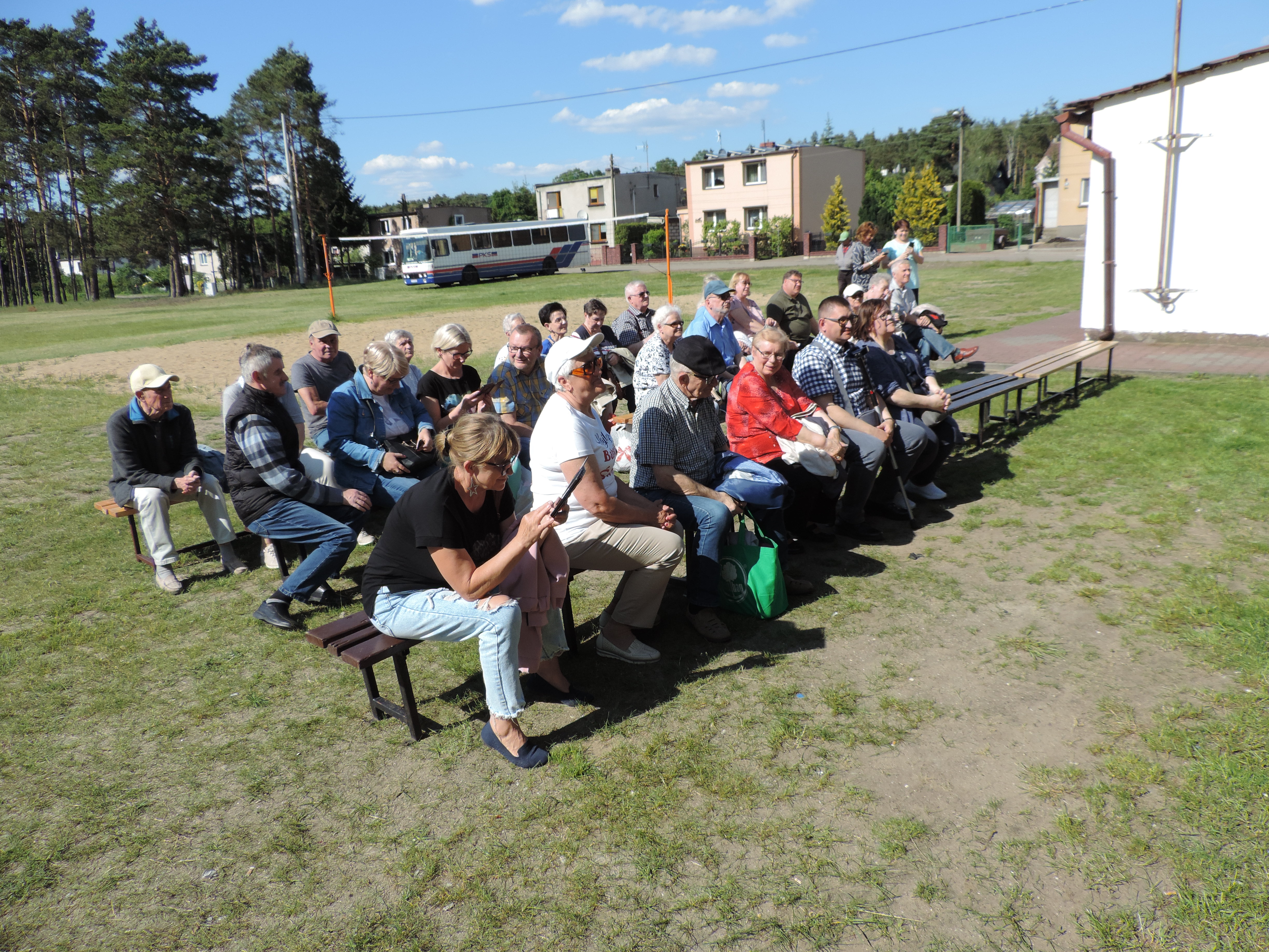 Na zdjęciu widać osoby siedzące na ławkach z PZN (Polskiego Związku Niewidomych).