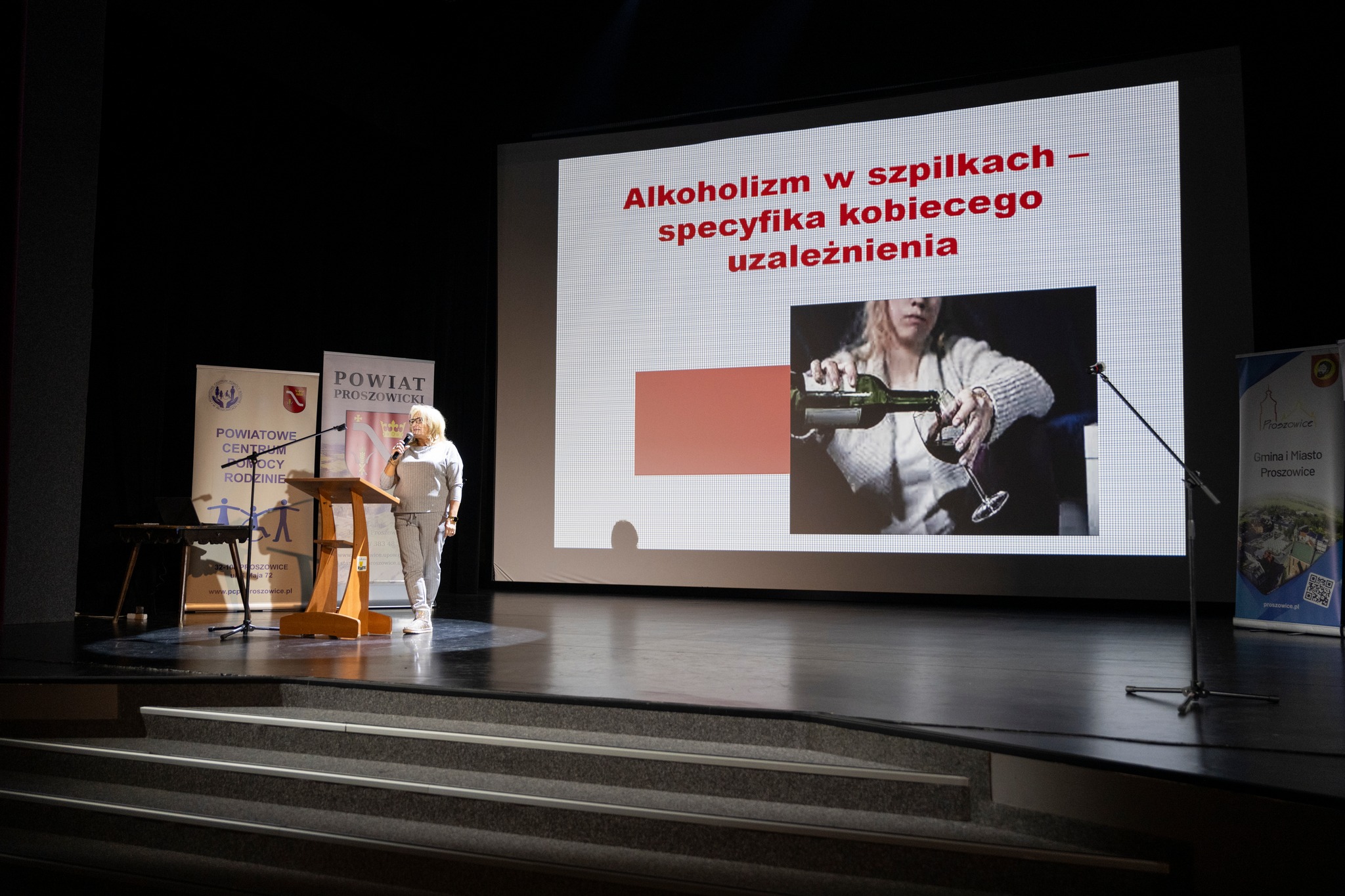Prelekcja Pani Beaty Wołkowicz Jasińskiej, w tle slajd z tematem prezentacji Alkoholizm w szpilkach - specyfika kobiecego uzależnienia