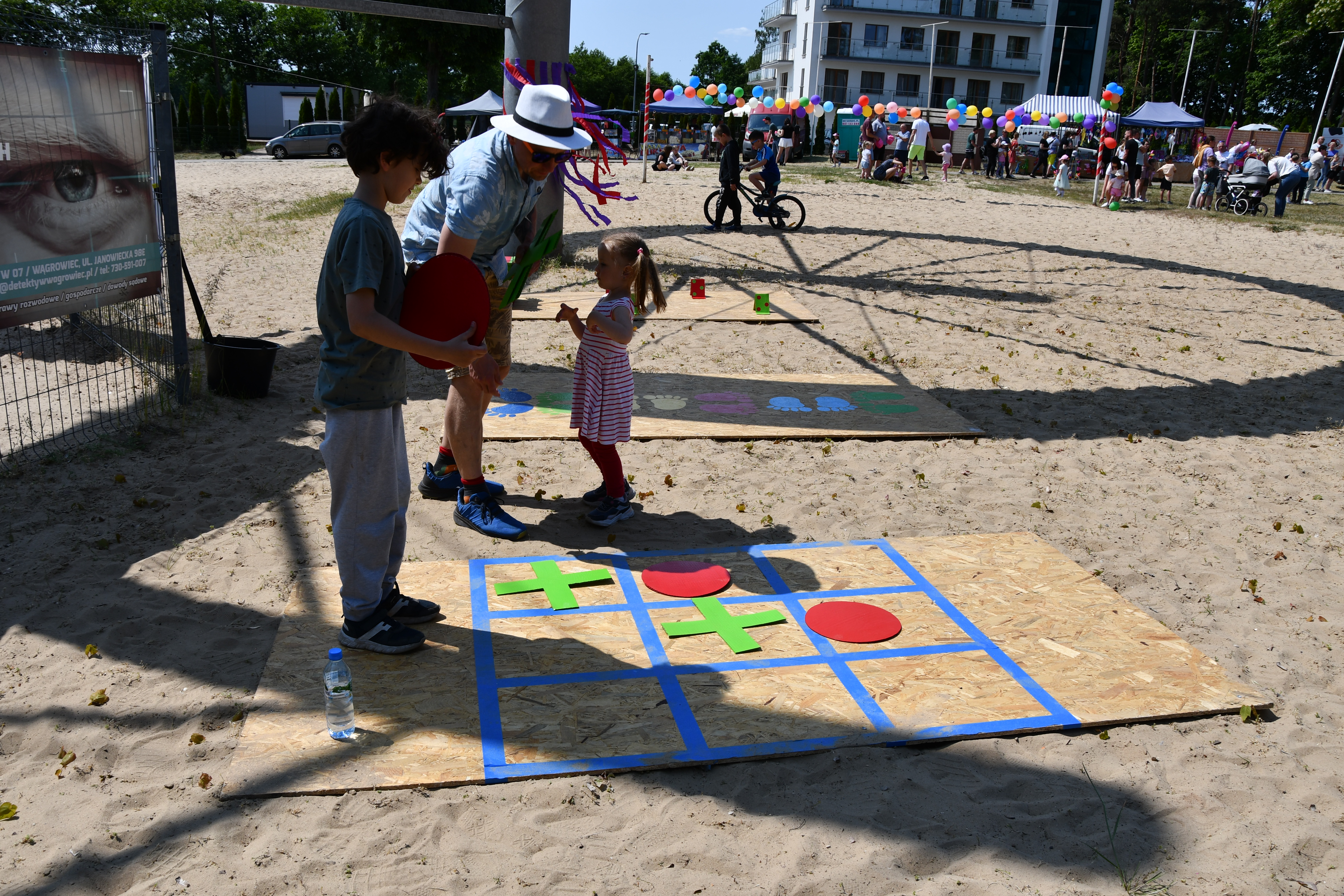 Dwójka dzieci wraz z jednym dorosłym grają w duże kółko i krzyżyk na ziemi na plaży w Margoninie.