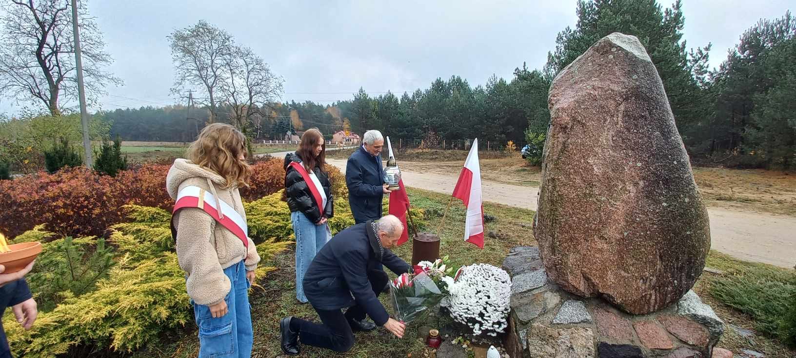 Przedstawiciele władz samorządowych oraz uczniowie podczas składania kwiatów przy kamieniu pamiątkowym w Bialymbłocie.