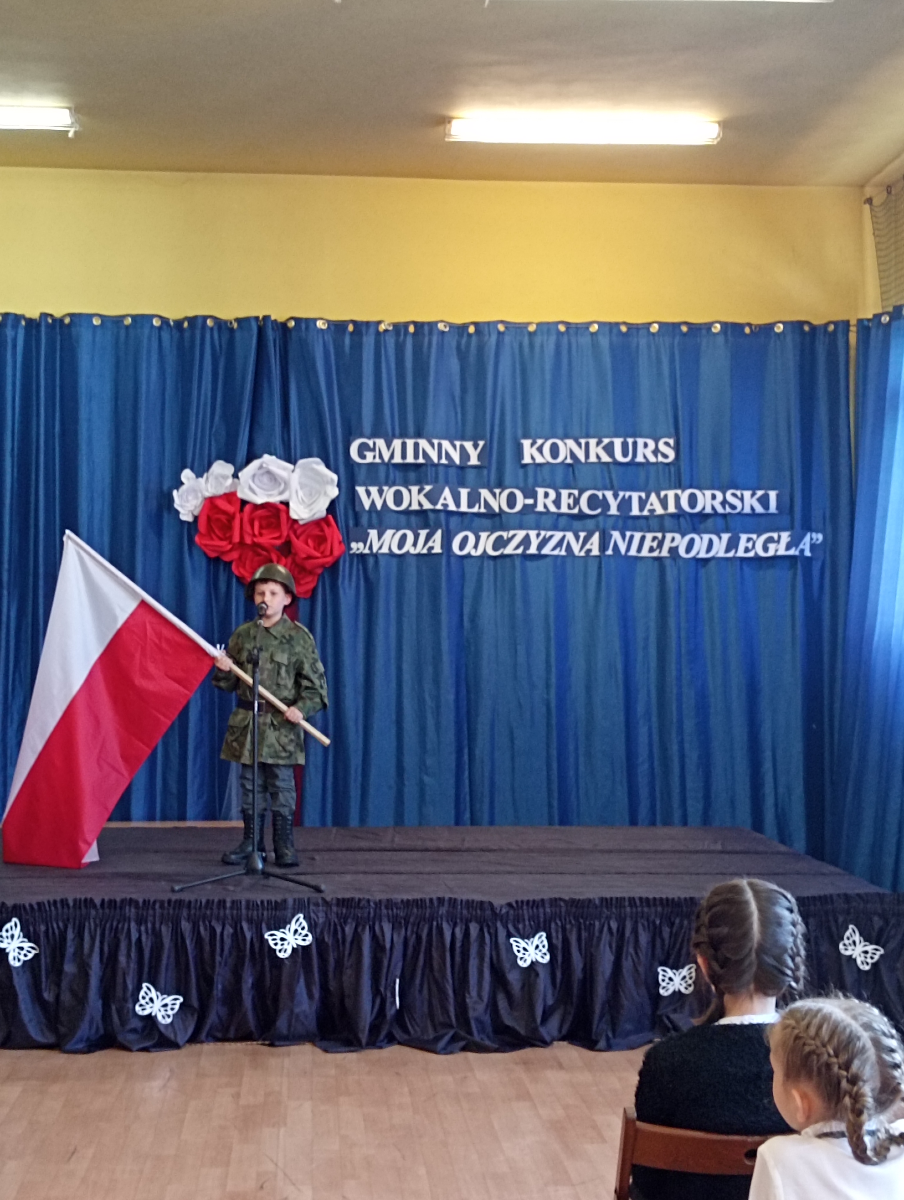 Chłopiec z ubraniu wojskowym trzyma polską flagę