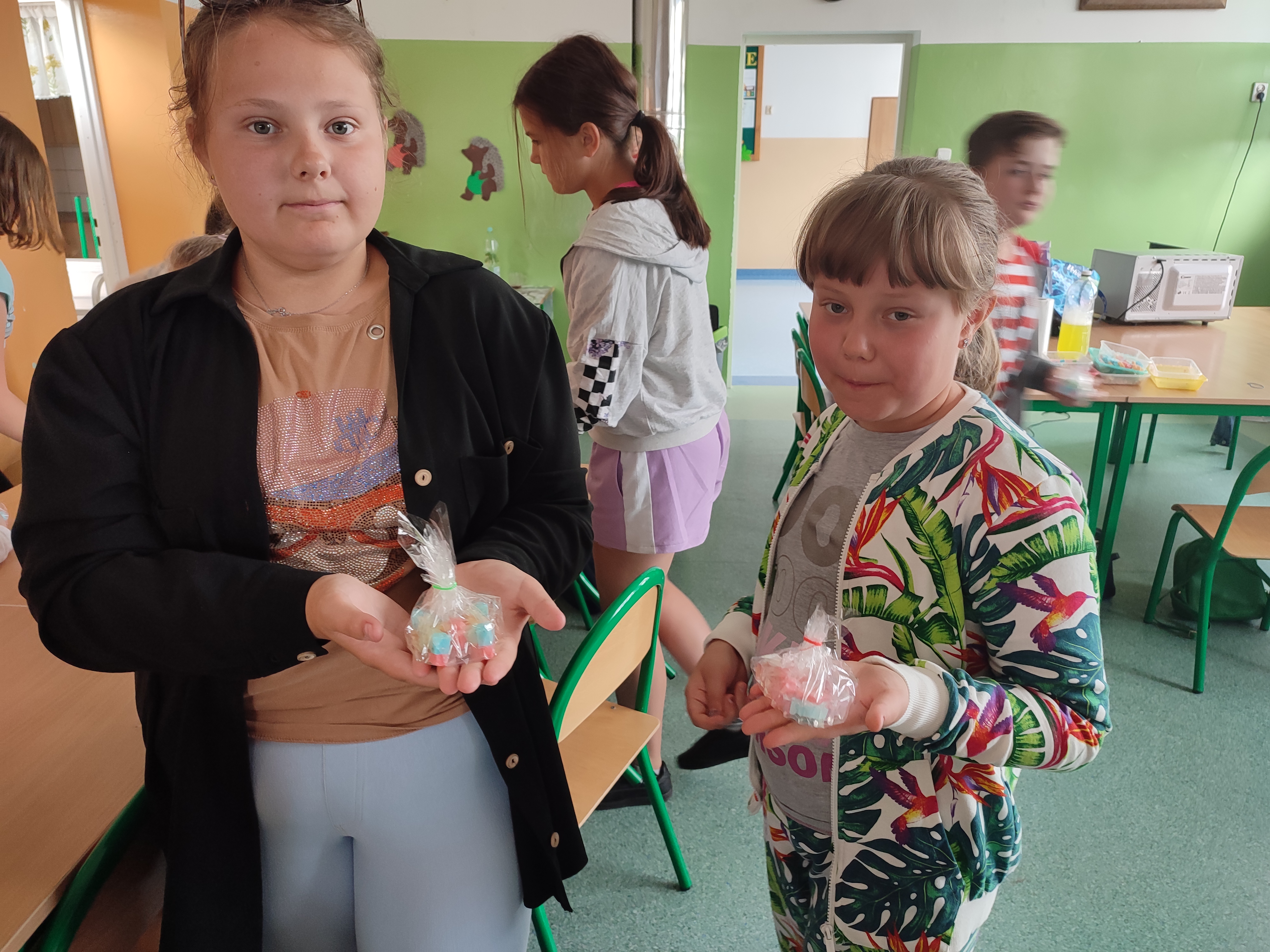 Zdjęcie przedstawia dwie dziewczynki prezentujące gotowe mydełka glicerynowe.